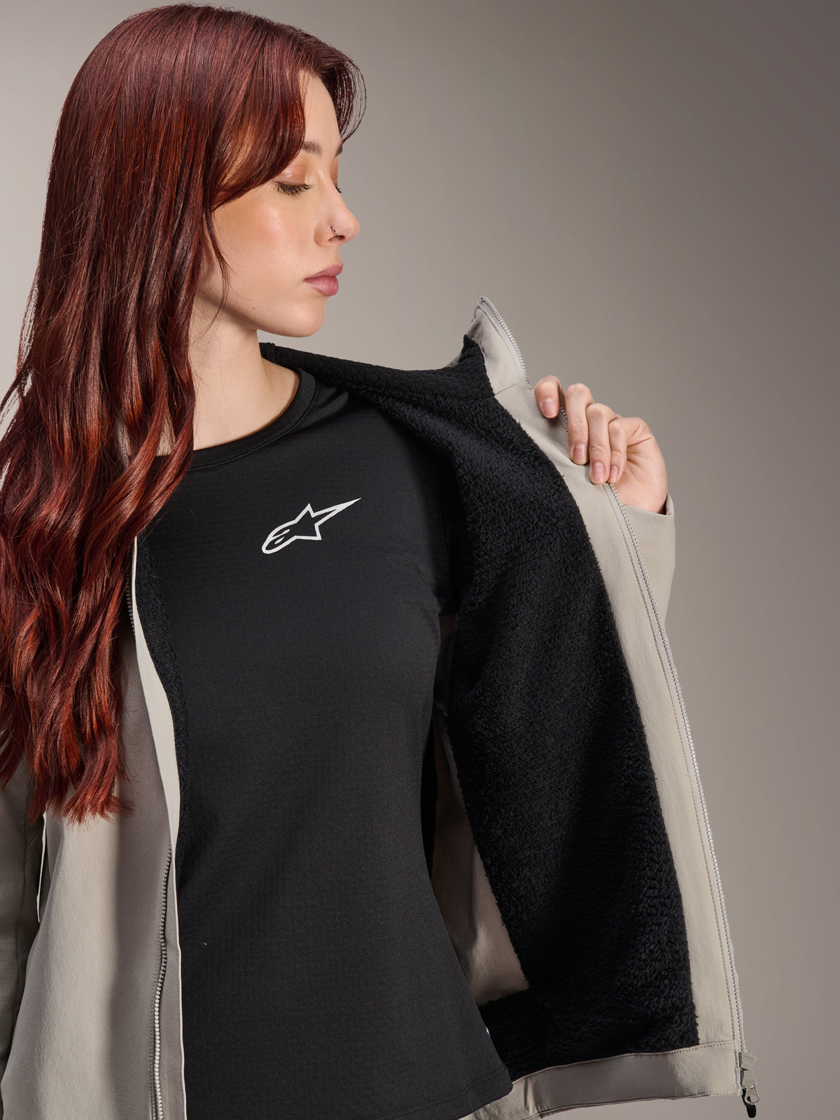 Donna che indossa la giacca termica Alpinestars Stella A-Dura in Titanium, che mostra la fodera in pile nero testurizzato, indossata sopra una t-shirt nera con logo a stella bianco, giacca leggera da mountain bike per condizioni fredde