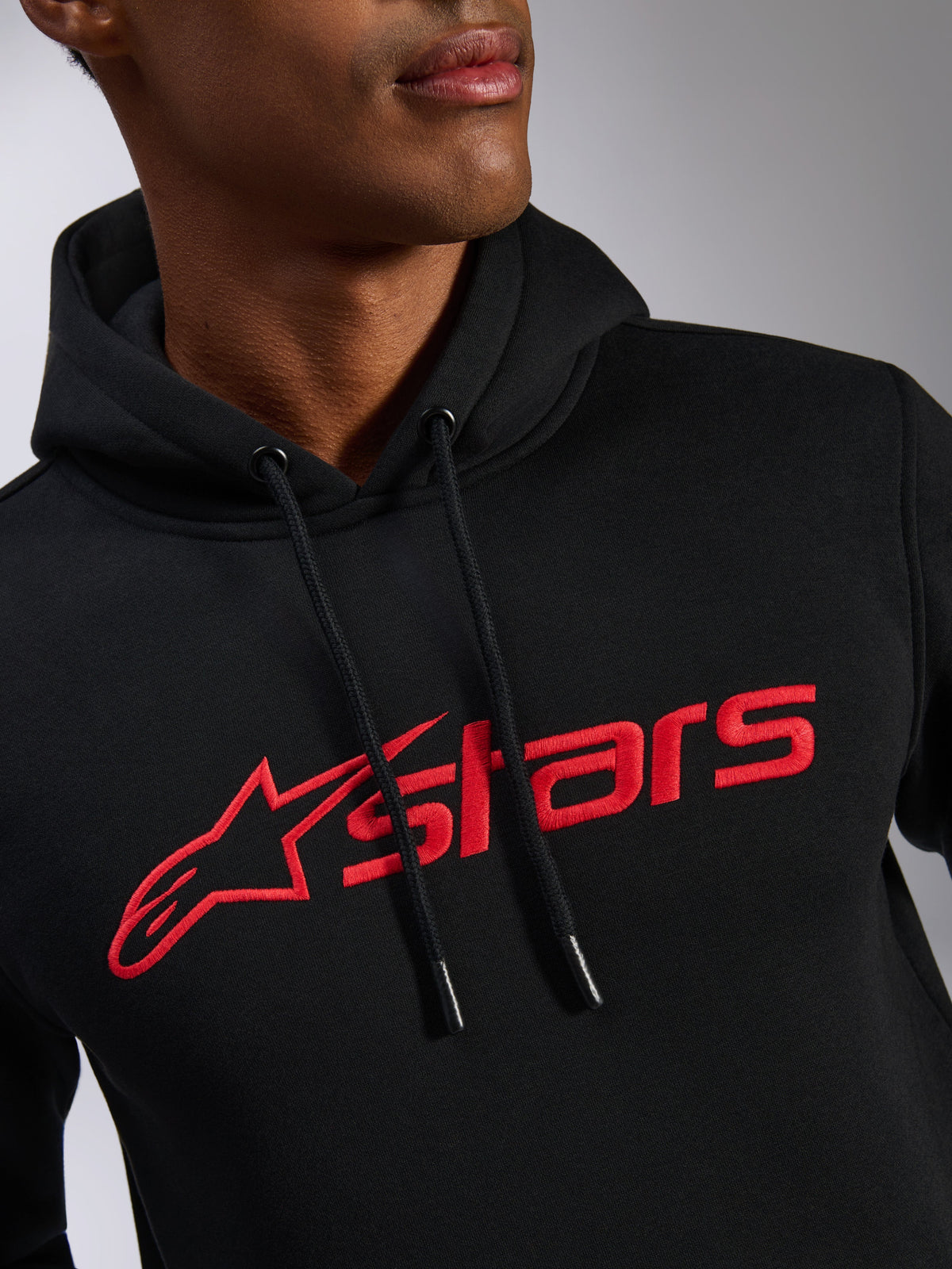 Felpa con cappuccio Alpinestars Blaze V3, primo piano del petto, tessuto in pile nero con stampa del logo lineare Alpinestars rosso, cappuccio con cordino ed estremità immerse, streetwear casual ispirato al motorsport