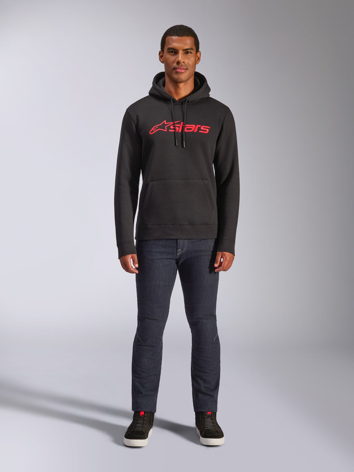 Felpa con cappuccio Alpinestars Blaze V3, streetwear casual, nero con logo Astars rosso, vista frontale, indossata da un modello con pantaloni in denim scuro e sneakers nere, design moderno in pile ispirato al motorsport