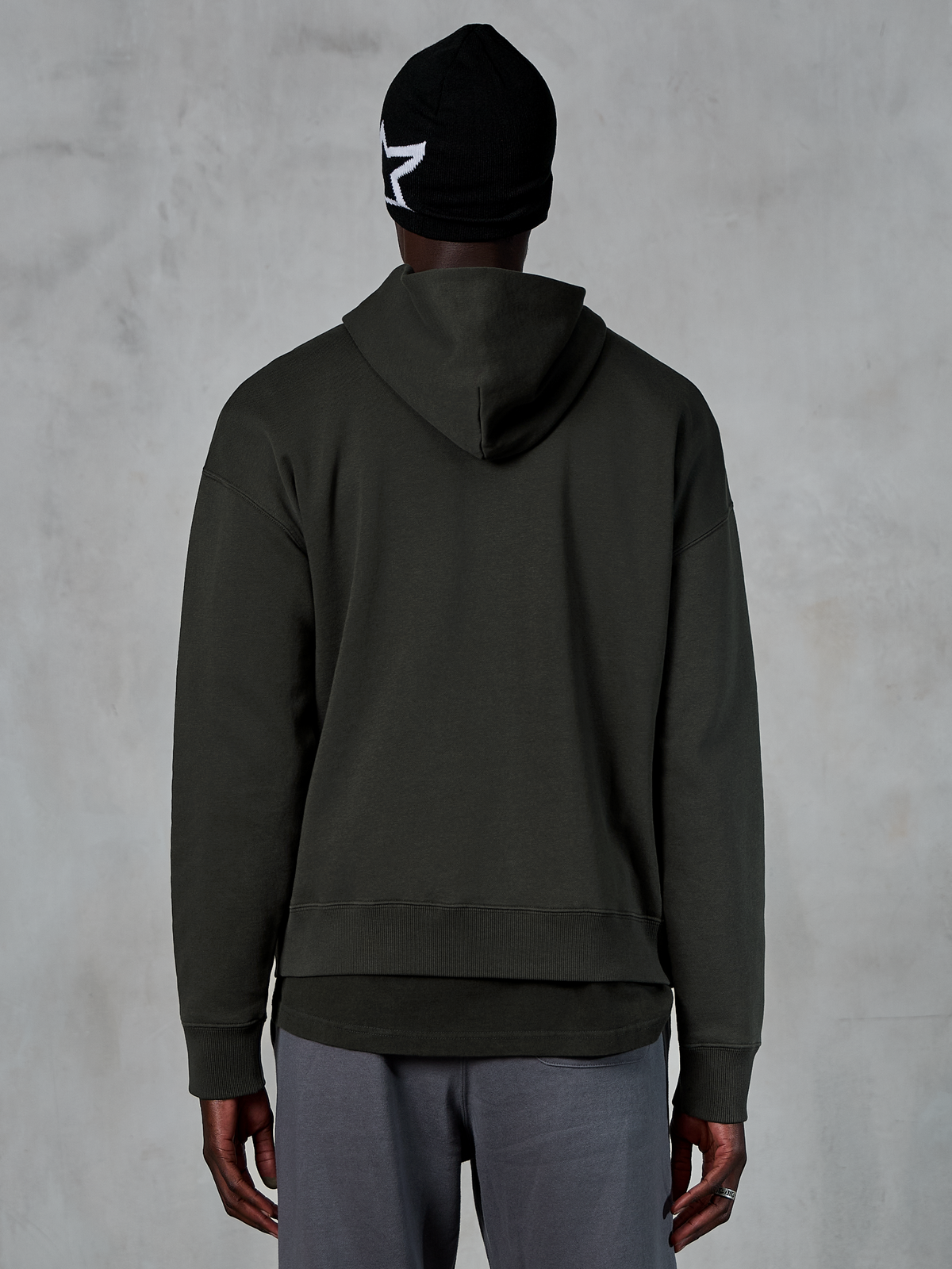 Alpinestars Essentials Ageless Hoodie, vista posteriore, Off Black, streetwear casual, modello che indossa un berretto nero con logo a stella bianca e pantaloni grigi, pile pregiato con finitura stone-wash