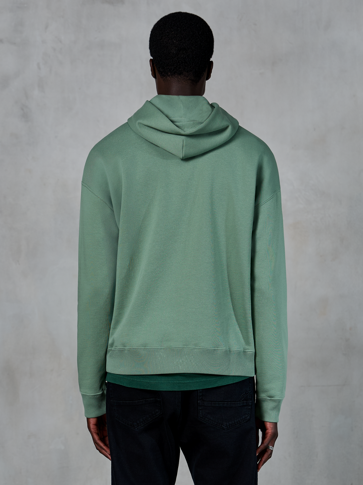 Felpa con cappuccio Alpinestars Essentials Ageless, abbigliamento sportivo casual, verde Cactus, vista posteriore su modello, finitura stone wash, abbinata a pantaloni neri, design lifestyle minimalista