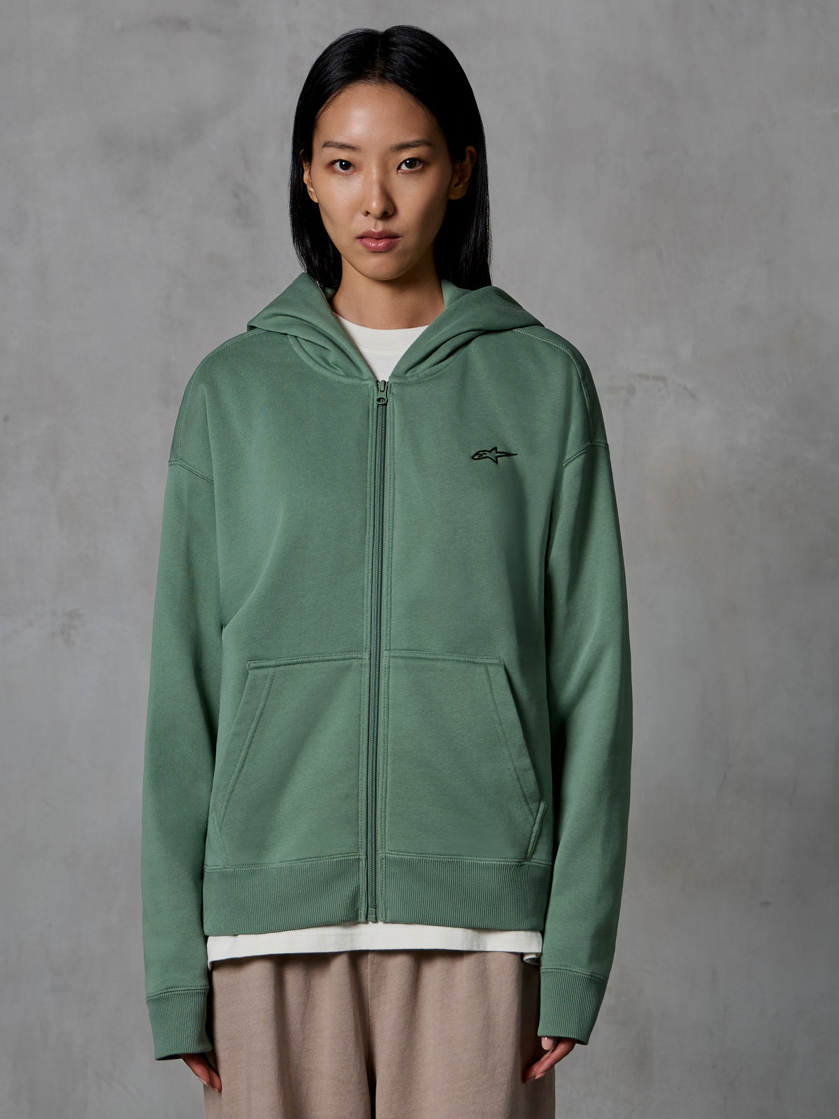 Felpa con cappuccio e zip Alpinestars Essentials Ageless, Verde Cactus, streetwear casual indossato da una modella, felpa in pile con zip e piccolo logo nero sul petto, tasche anteriori, vestibilità rilassata per l'uso quotidiano
