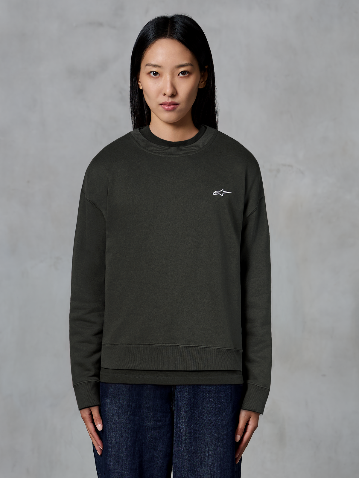 Alpinestars Essentials Ageless Crew, felpa girocollo premium, Off Black, con un piccolo logo Alpinestars bianco sul petto, stile streetwear casual, indossata da una modella con jeans scuri