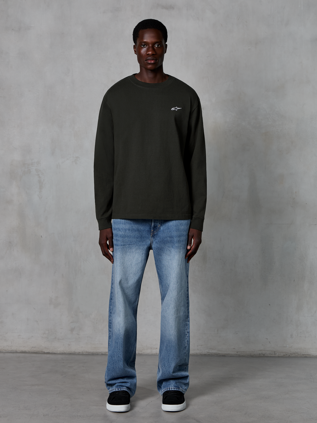 Alpinestars Essentials Ageless LS Tee, maglia a maniche lunghe, nero, con piccolo logo a stella bianco sul petto, vestibilità rilassata, streetwear casual ispirato al motorsport, abbinata a jeans azzurro chiaro