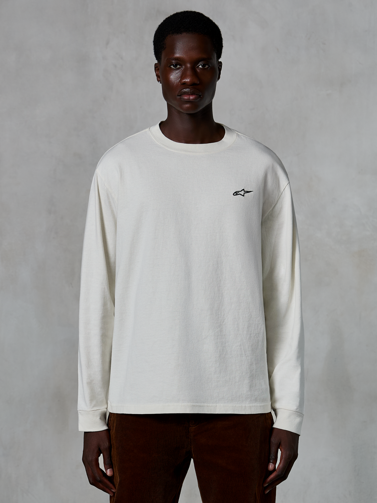 Alpinestars Essentials Ageless LS Tee, t-shirt a maniche lunghe, bianco sporco, piccolo logo a stella nero sul petto, streetwear casual, vestibilità rilassata, indossata da un modello
