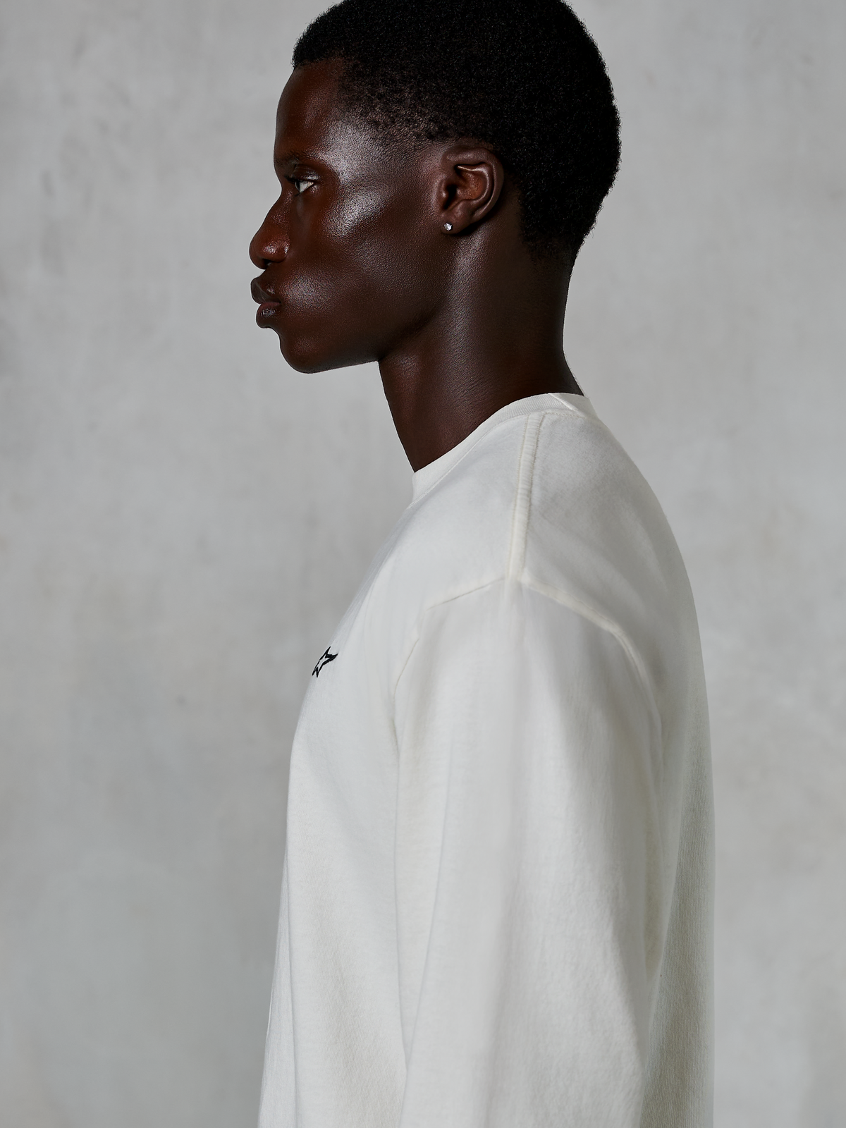 Alpinestars Essentials Ageless LS Tee, maglia a maniche lunghe, Off White, vista di profilo di un uomo che indossa la maglia dalla vestibilità rilassata, con piccolo logo nero sul petto, abbigliamento lifestyle casual ispirato al motorsport