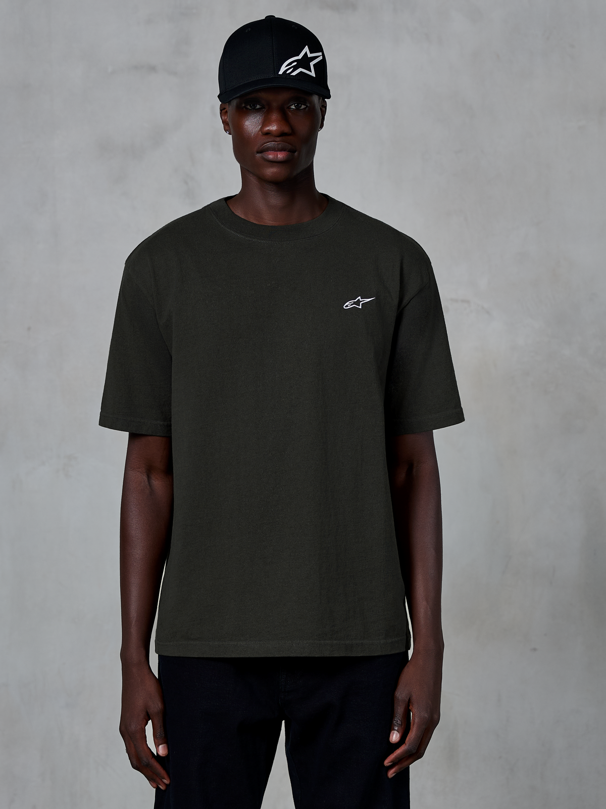 Alpinestars Essentials Ageless SS Tee, t-shirt a maniche corte, nero, indossata da un modello con cappellino nero con logo, piccolo logo Alpinestars bianco sul petto, streetwear casual ispirato al motorsport