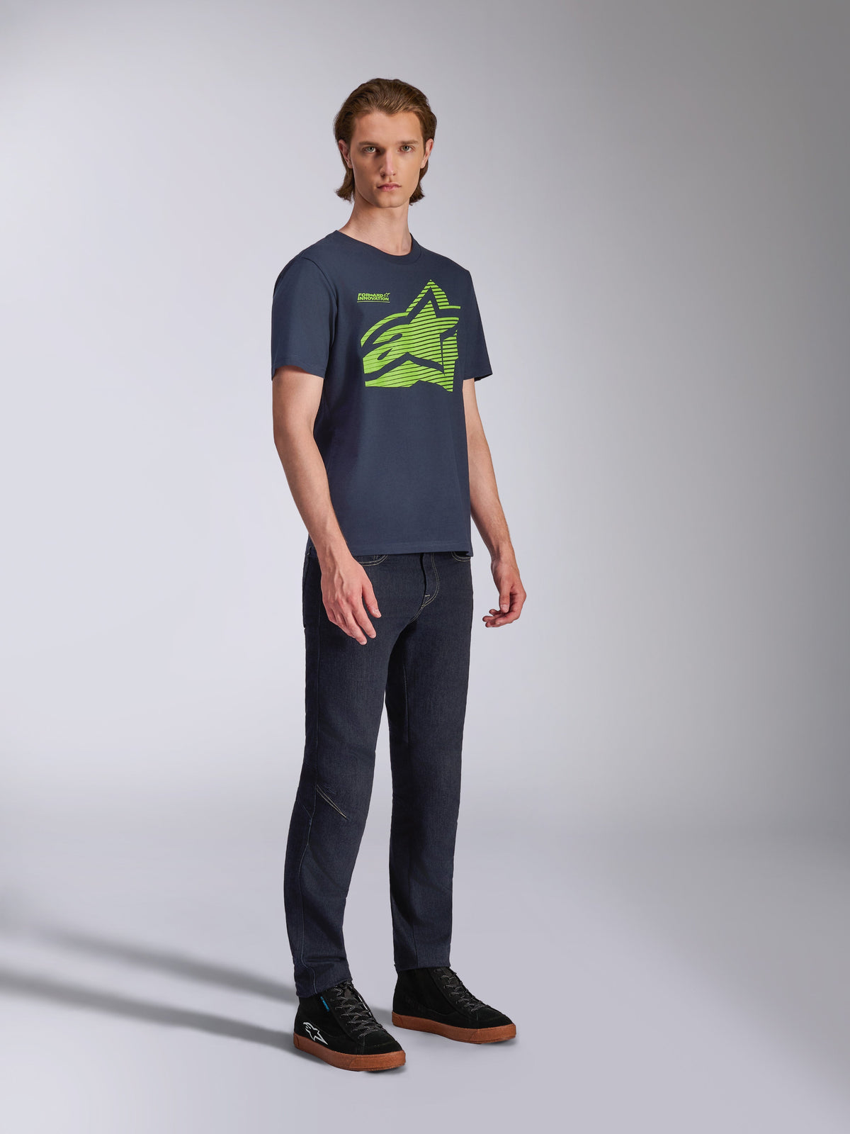 Alpinestars Fasting CSF Tee, t-shirt a maniche corte, blu navy, logo Astars geometrico verde lime, indossata con jeans scuri e sneakers nere, streetwear casual ispirato al motorsport