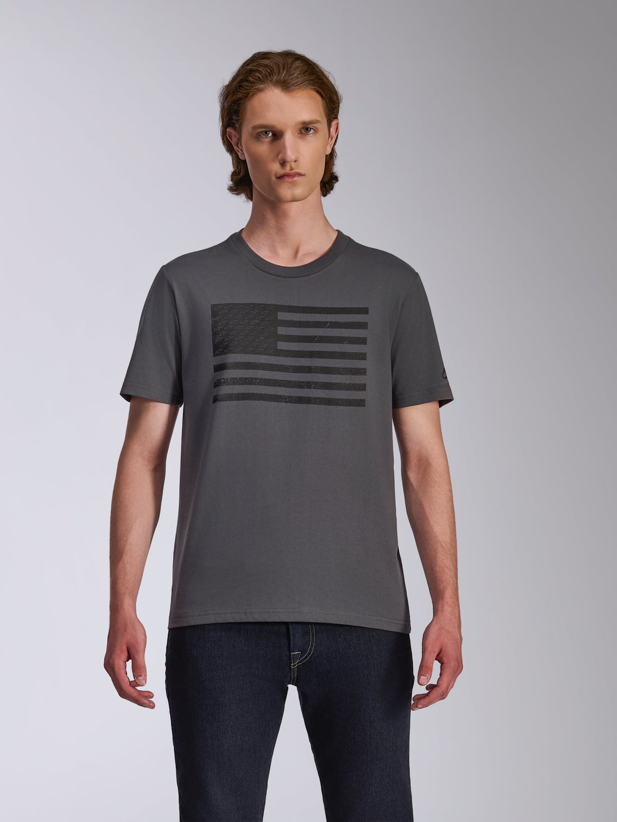 Alpinestars Waving CSF Tee, t-shirt a maniche corte, colore Charcoal, con grafica logo Blaze nera ispirata a una bandiera sul petto, indossata da un modello con jeans scuri, abbigliamento streetwear casual stile motorsport