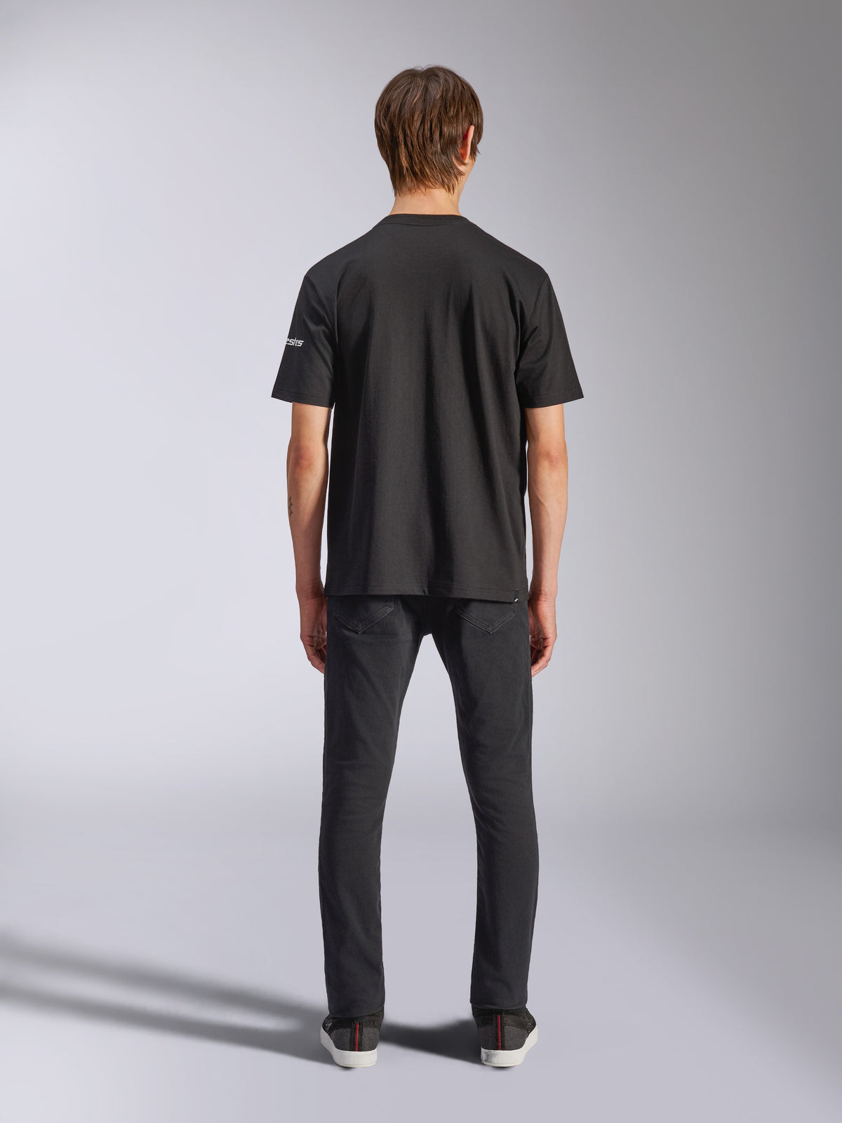 Alpinestars Frontal CSF Tee, maglietta a maniche corte, nero, vista posteriore su modello che indossa jeans neri, streetwear casual ad alte prestazioni con dettaglio del piccolo logo bianco sulla manica