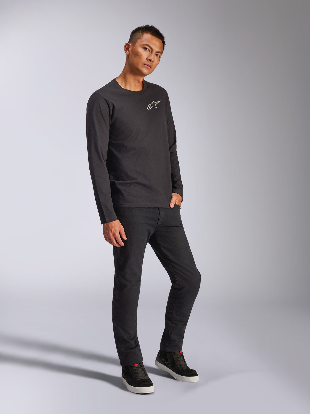 Alpinestars Trackside CSF Tee, maglia a maniche lunghe, nero, logo Astars bianco sul petto, indossata da un modello con pantaloni neri e sneakers, streetwear casual ispirato al motorsport