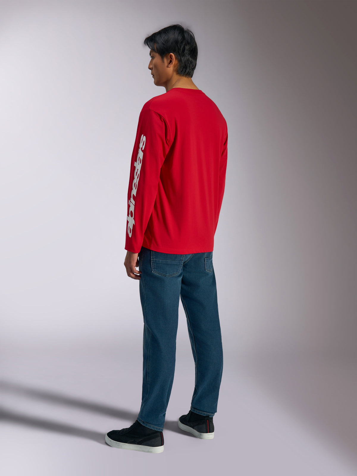 Alpinestars Trackside CSF Tee, t-shirt a maniche lunghe, rossa, con logo Alpinestars bianco verticale sulla manica, indossata da un modello con jeans blu e sneakers nere, streetwear casual ispirato al motorsport