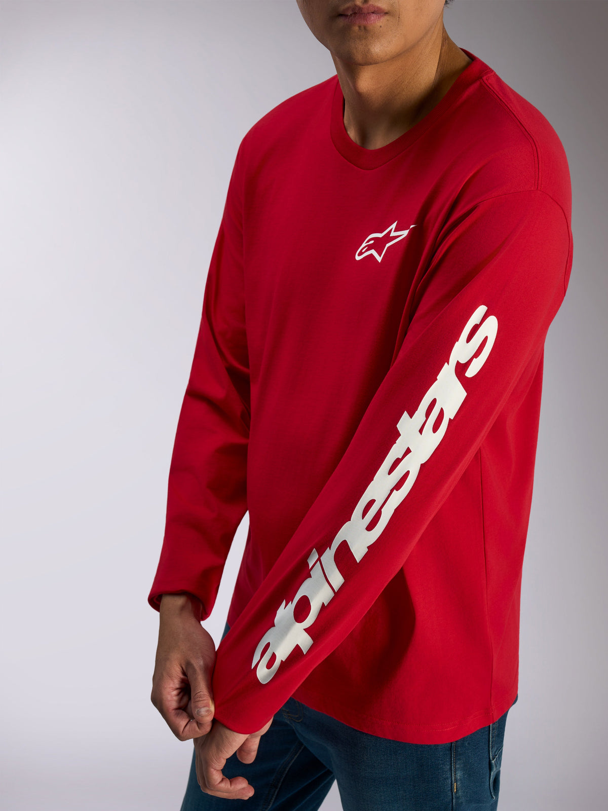 Alpinestars Trackside CSF Tee, maglia a maniche lunghe, rossa, logo Alpinestars bianco sul petto e vistosa scritta sulla manica, streetwear casual da motorsport indossata con jeans blu