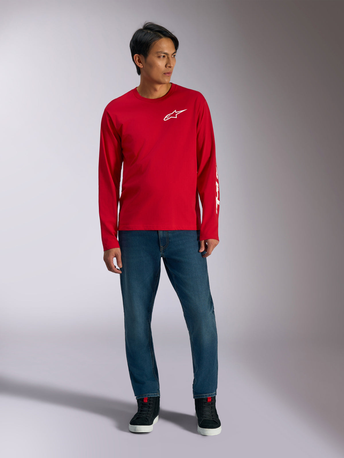 Alpinestars Trackside CSF Tee, maglia a maniche lunghe, rossa con logo Alpinestars bianco, foto lifestyle indossata con jeans blu e sneakers nere, abbigliamento sportivo casual ispirato al motorsport