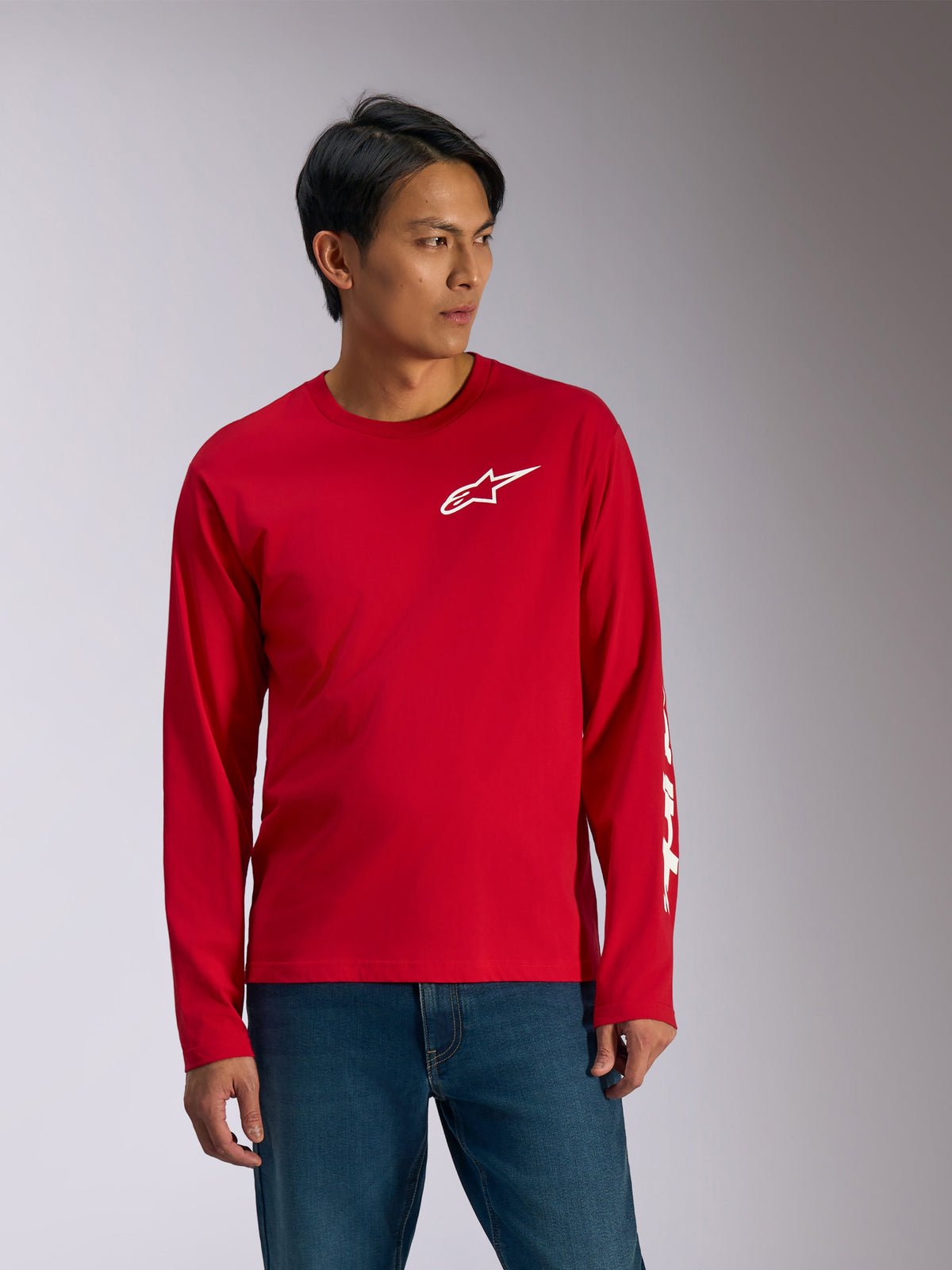 Alpinestars Trackside CSF Tee, t-shirt a maniche lunghe, rosso con grafiche bianche, logo Alpinestars a stella bianco sul petto e scritta bianca sulla manica, indossata con jeans blu, abbigliamento sportivo casual ispirato al motorsport
