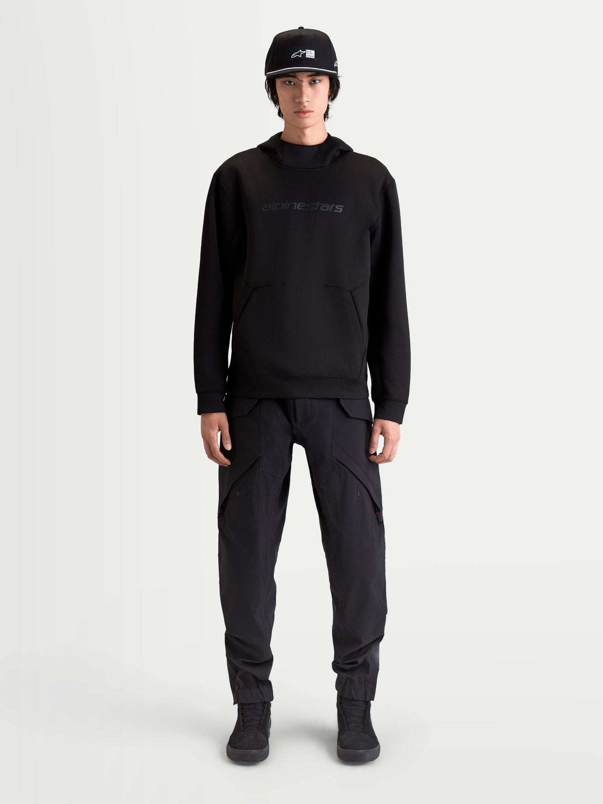 Alpinestars felpa con cappuccio Datrix, pullover sportswear premium da uomo, nera, branding Alpinestars HD tono su tono, pile tri-blend double-face e tasca con dettaglio a freccia, indossata da un modello per uno stile ispirato al motorsport
