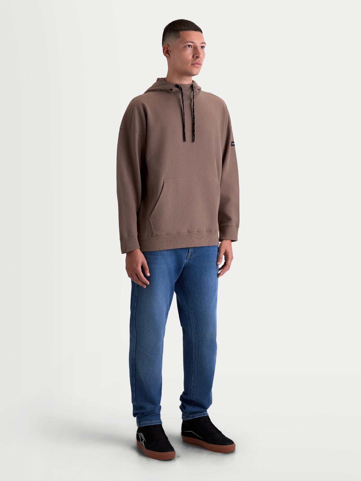 Alpinestars Felpa con cappuccio Camino Textured Oversized, felpa sportswear da uomo, marrone, in pile di twill testurizzato, vestibilità ampia, collo alto e tasca a marsupio, indossata da un modello con jeans, stile casual motorsport