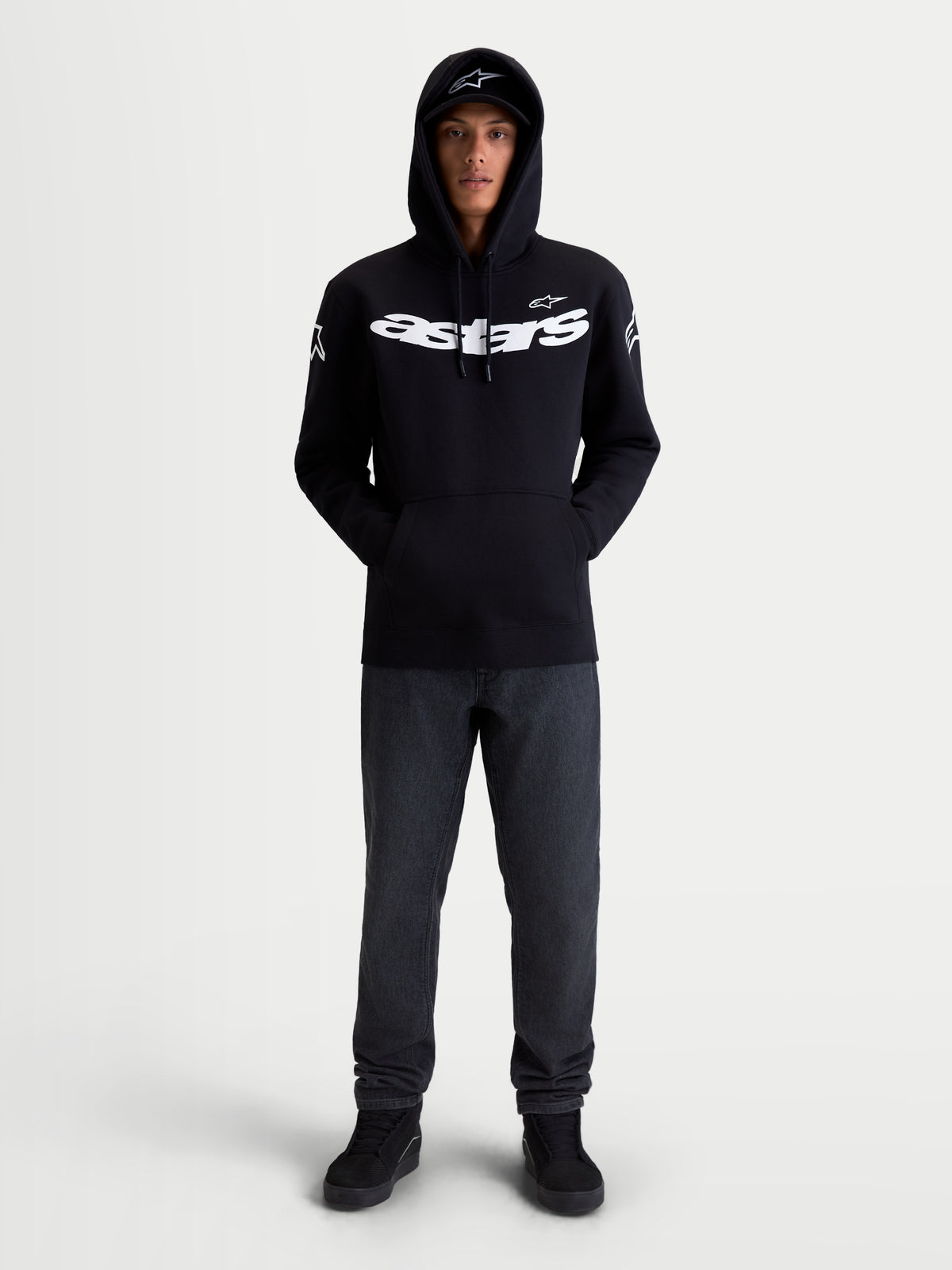 Alpinestars Felpa con cappuccio Velocifier, pullover in pile da sportswear da moto unisex, nera e bianca, in misto cotone e poliestere riciclato, con grande scritta Astars sul petto e loghi sulle spalle, vista frontale su modello per abbigliamento casual off-bike.