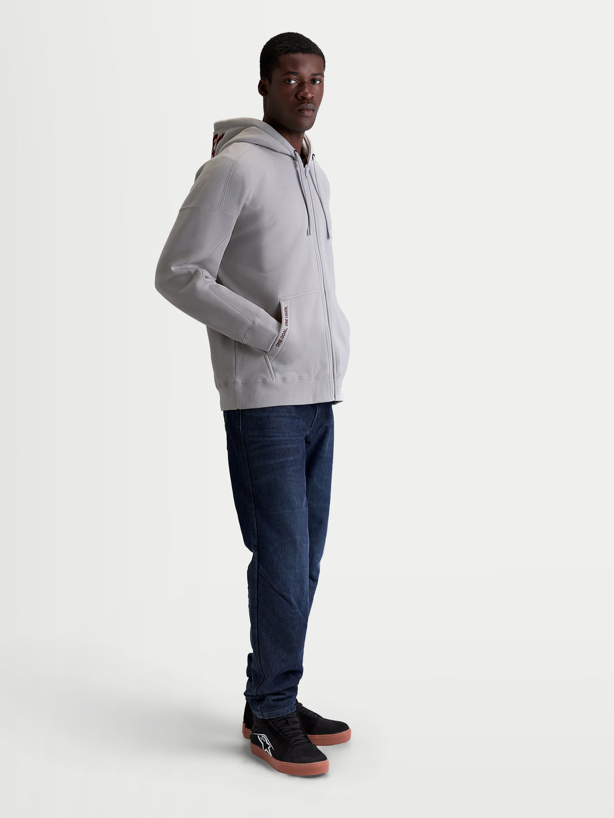 Alpinestars felpa con cappuccio Pioneer Oversize, felpa sportswear da uomo con zip in grigio cemento, vestibilità oversize, cerniera Vislon, tasca a marsupio con ricamo One Goal One Vision, cappuccio foderato, indossata con jeans e scarpe sportive