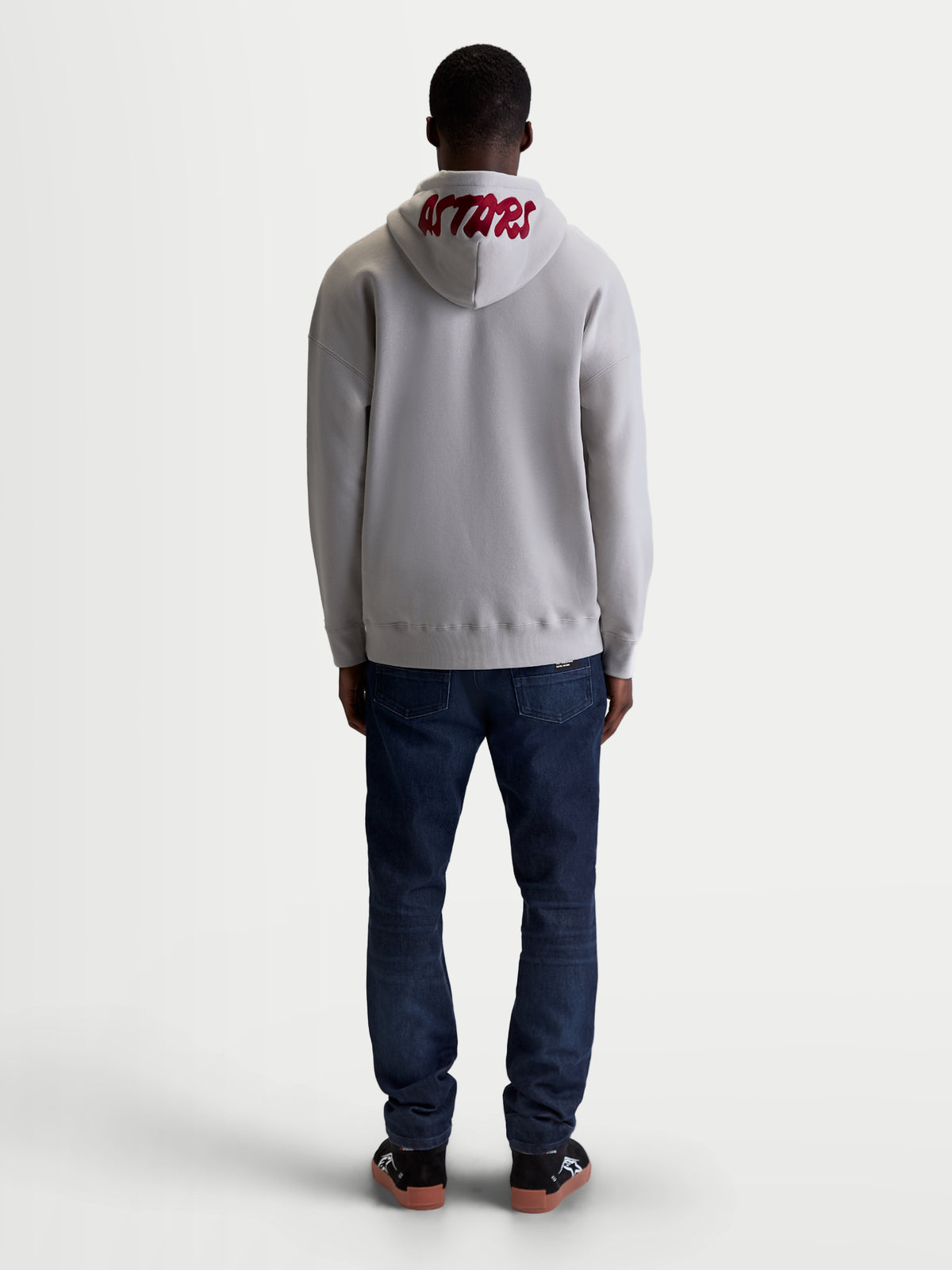 Alpinestars Felpa con cappuccio Pioneer Oversize, sportswear casual da uomo, grigio cemento e rosso, vista posteriore su modello con logo ASTARS ricamato sul cappuccio e vestibilità oversize rilassata.