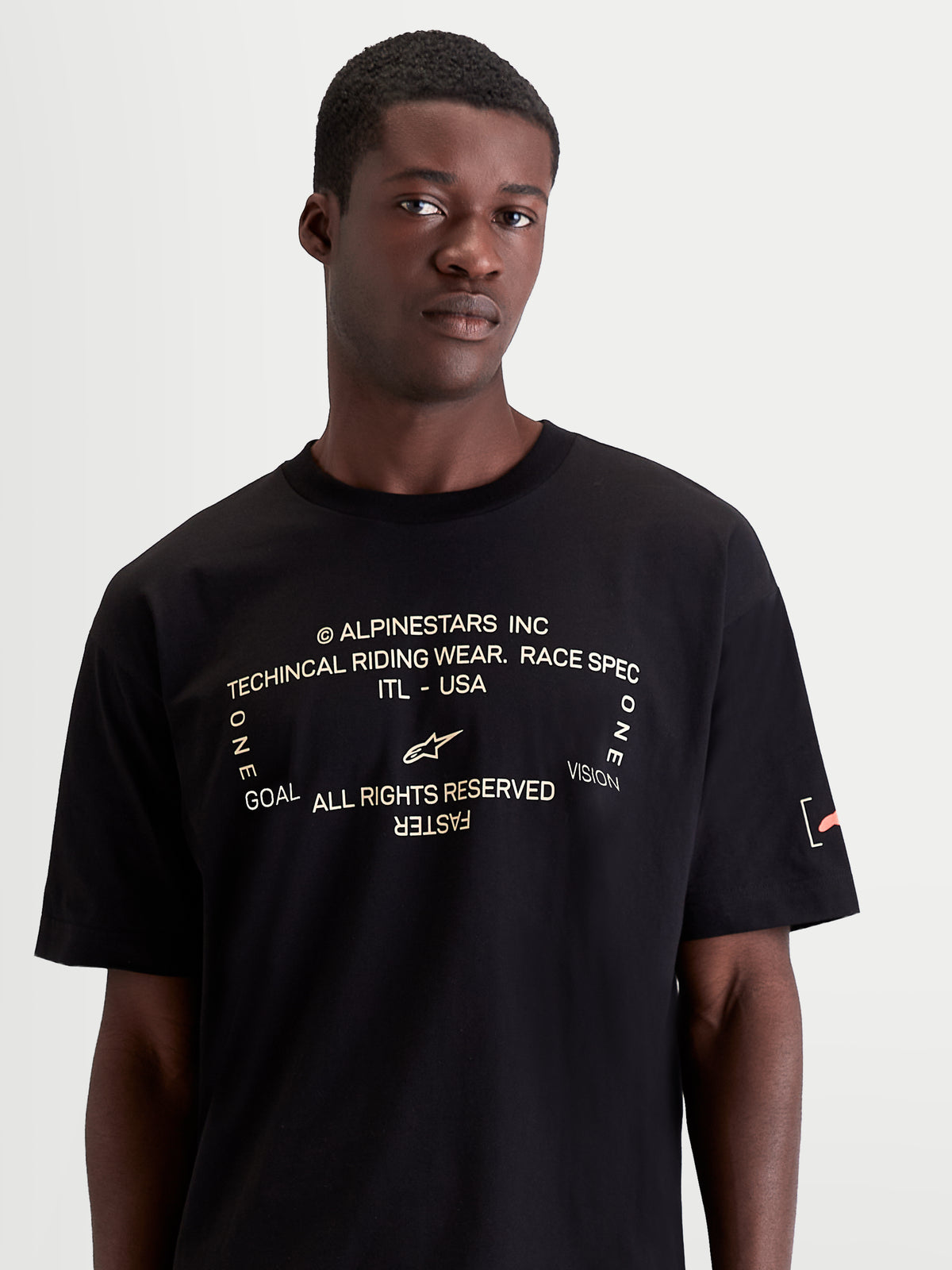Alpinestars Maglietta Infinity Oversized CSF, maglietta a maniche corte da uomo nera, fit oversized, grafica frontale bianca con logo e scritta One Goal. One Vision., logo arancione sulla manica, stile sportswear casual