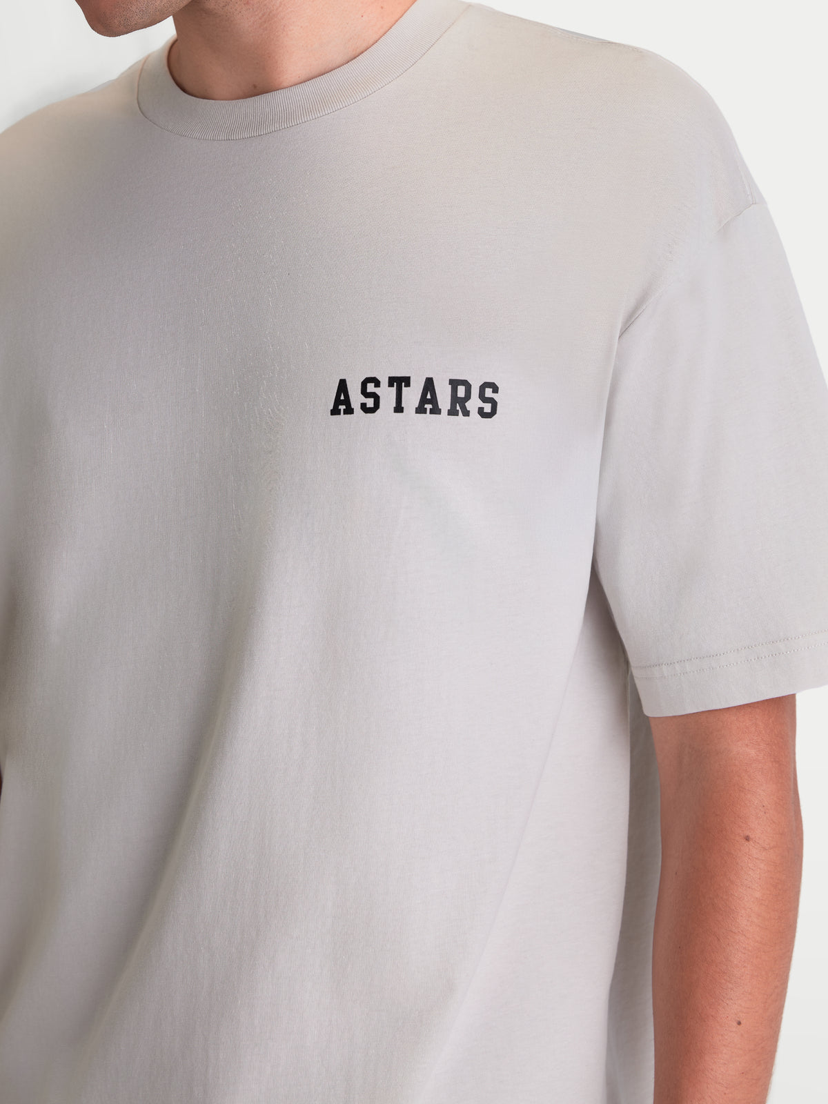 Alpinestars Maglietta Latitude Oversized CSF, maglietta a maniche corte grigio cemento con scritta ASTARS nera sul petto, vestibilità ampia e rilassata, sportswear casual, vista su modello.