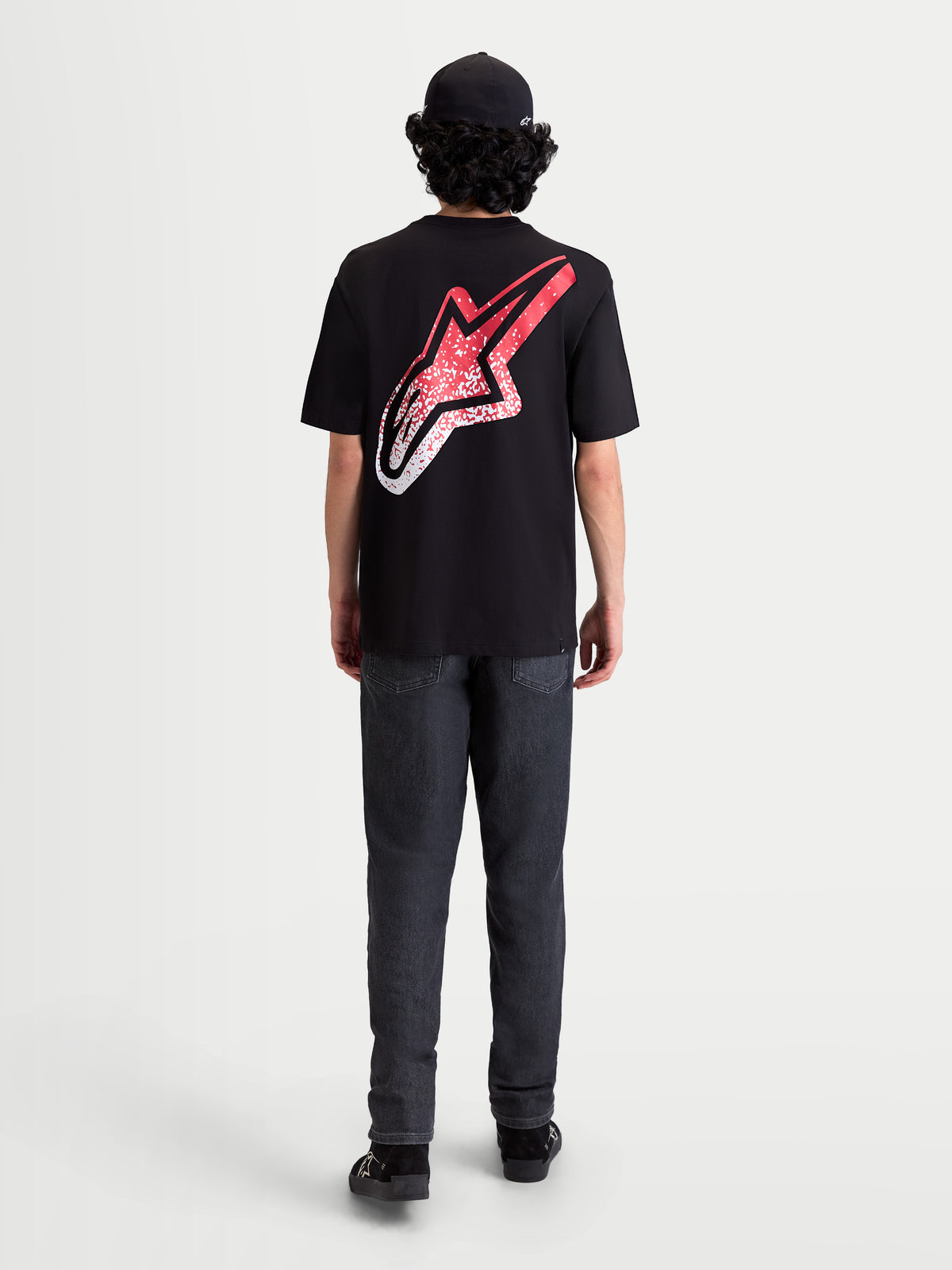 Alpinestars Maglietta Meteor CSF, maglietta a maniche corte nera, vista posteriore su modello con grande logo Astars sulla schiena, grafica sfumata rossa e bianca d'ispirazione MX, stile sportswear casual motorsport.