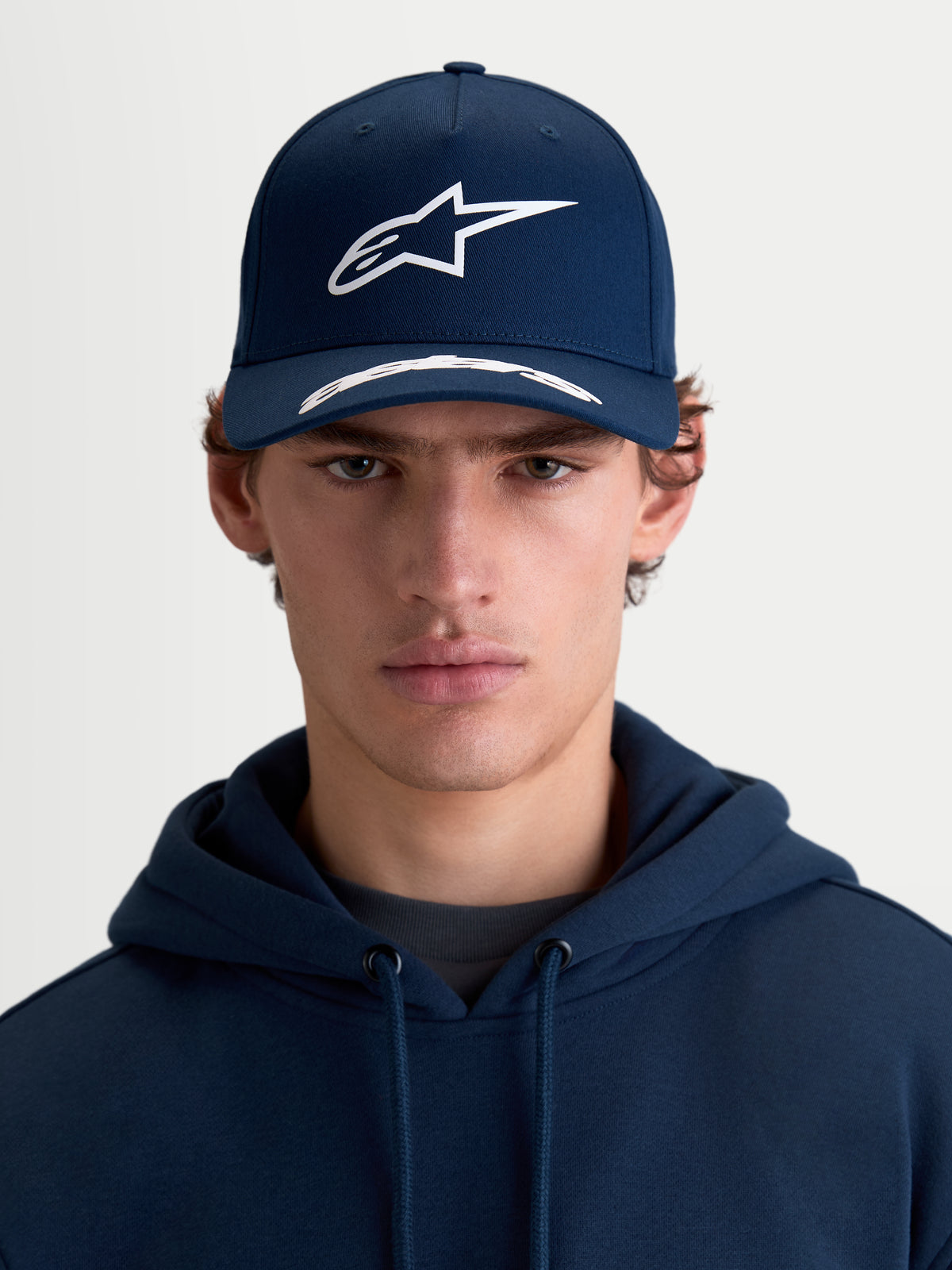 Alpinestars cappello Arclight, cappello sportswear con visiera curva, blu navy e bianco, vista frontale su modello, corona strutturata, logo Astars in rilievo puff print e twill di cotone premium