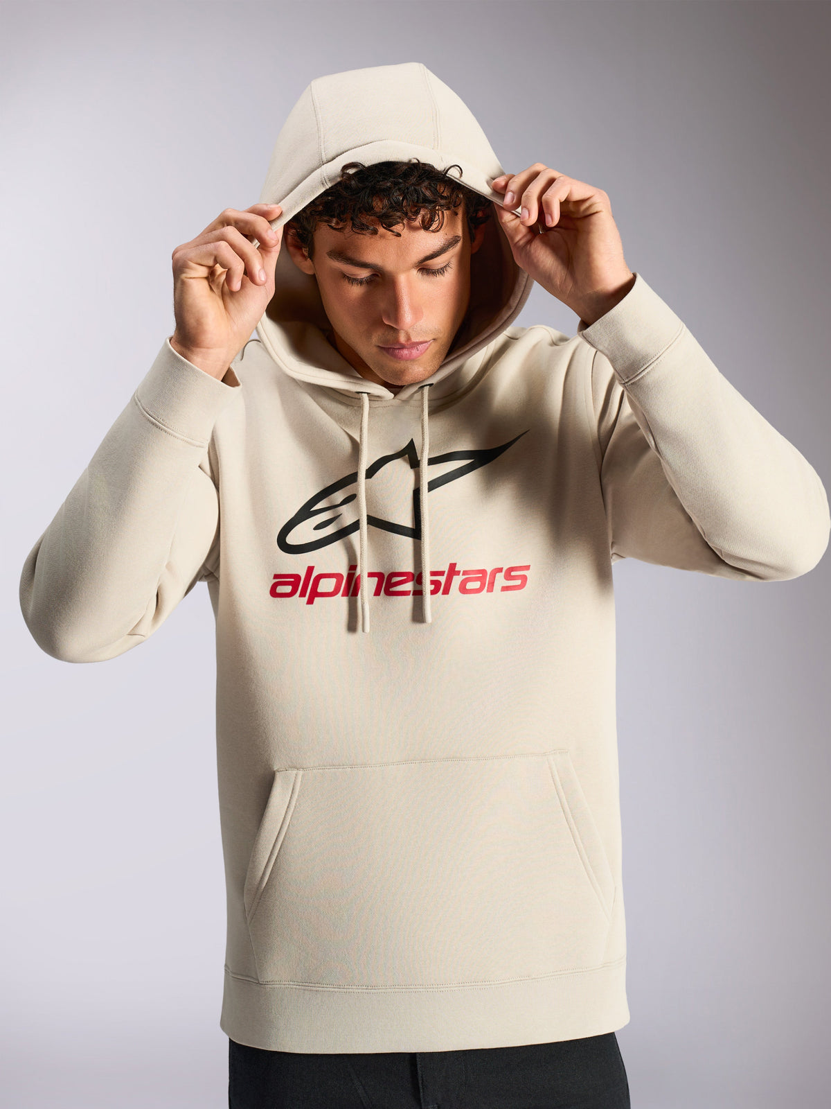 Alpinestars Always V3 Hoodie, modello che indossa una felpa pullover bianco sporco, logo lineare frontale nero e rosso, cappuccio con cordino, tasca a marsupio, streetwear casual ispirato al motorsport