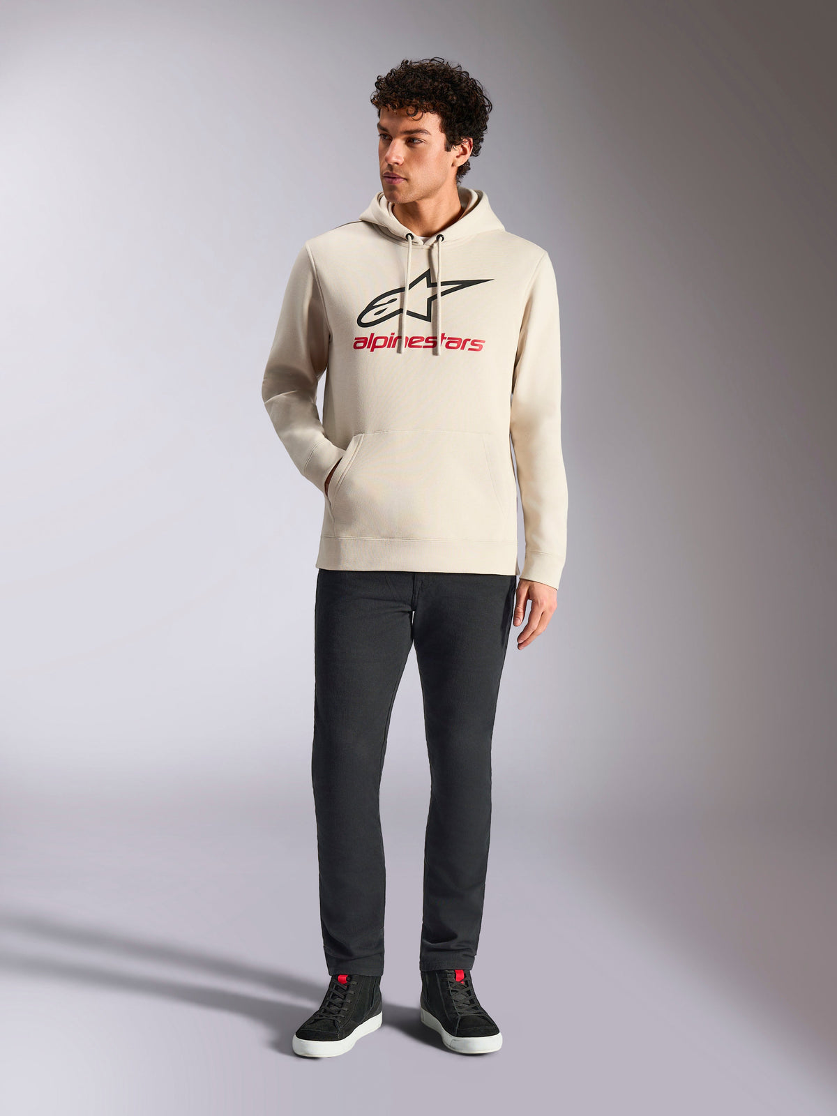 Alpinestars Always V3 Hoodie, streetwear casual, bianco sporco con logo a stella nero e scritte rosse, cappuccio con coulisse, maniche lunghe, indossata da modello uomo con pantaloni neri e sneaker nere