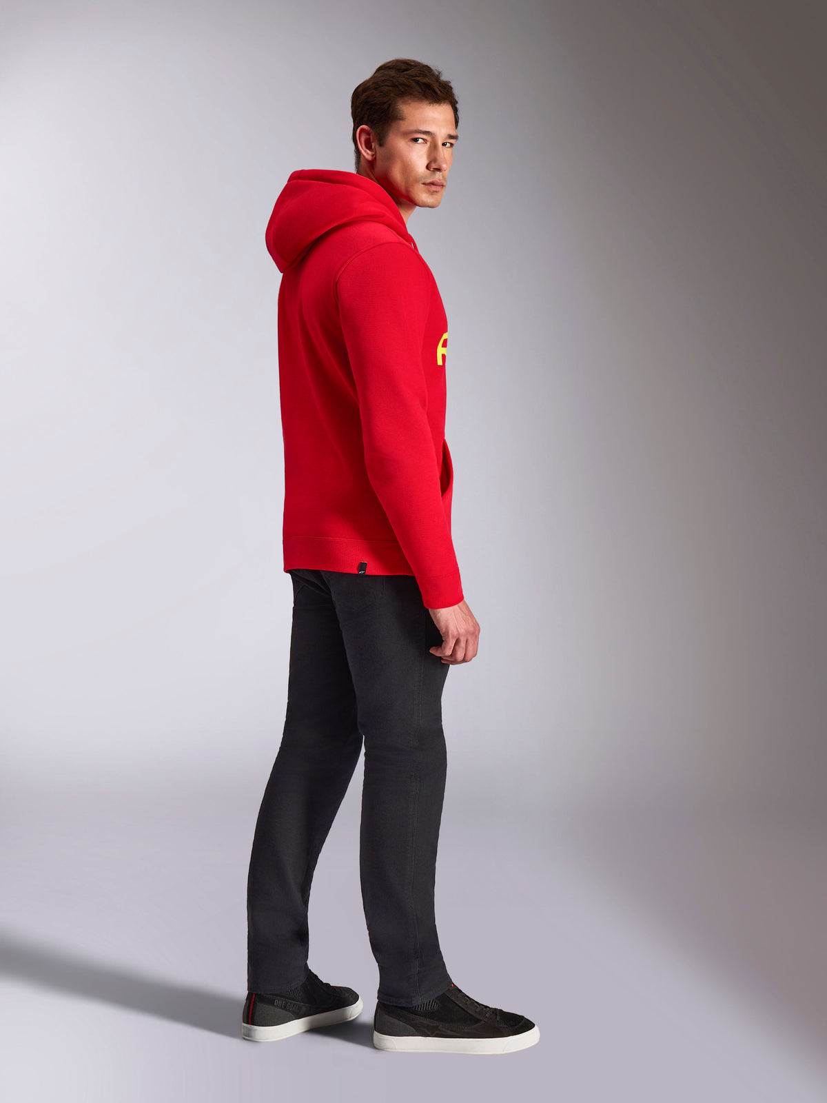 Alpinestars Ride V3 Hoodie, abbigliamento sportivo casual, rosso con marchio giallo alta visibilità, modello che indossa la felpa rossa con pantaloni neri e sneaker, vista di profilo, design pullover in pile con polsini e orlo a coste.