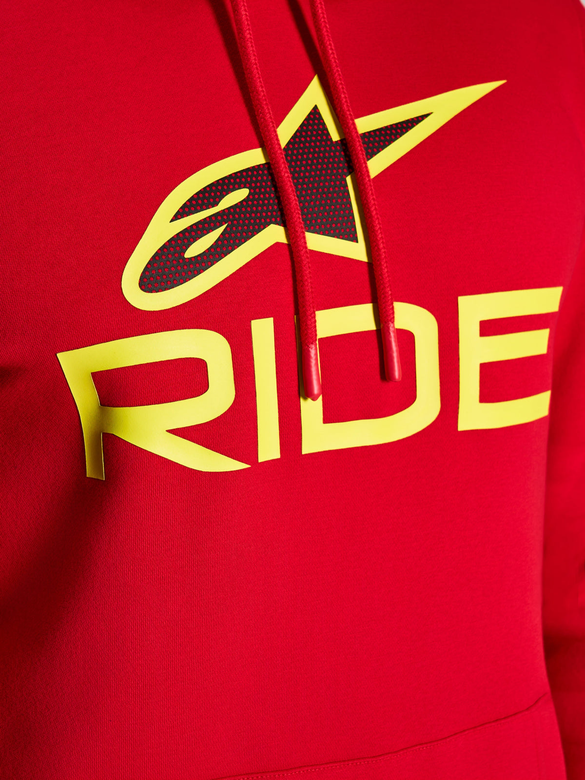 Alpinestars Ride V3 Hoodie, primo piano della grafica sul petto, rossa con scritta RIDE in giallo alta visibilità e logo a stella nero con stampa perforata, cordini rossi con estremità immerse, abbigliamento casual streetwear in pile premium