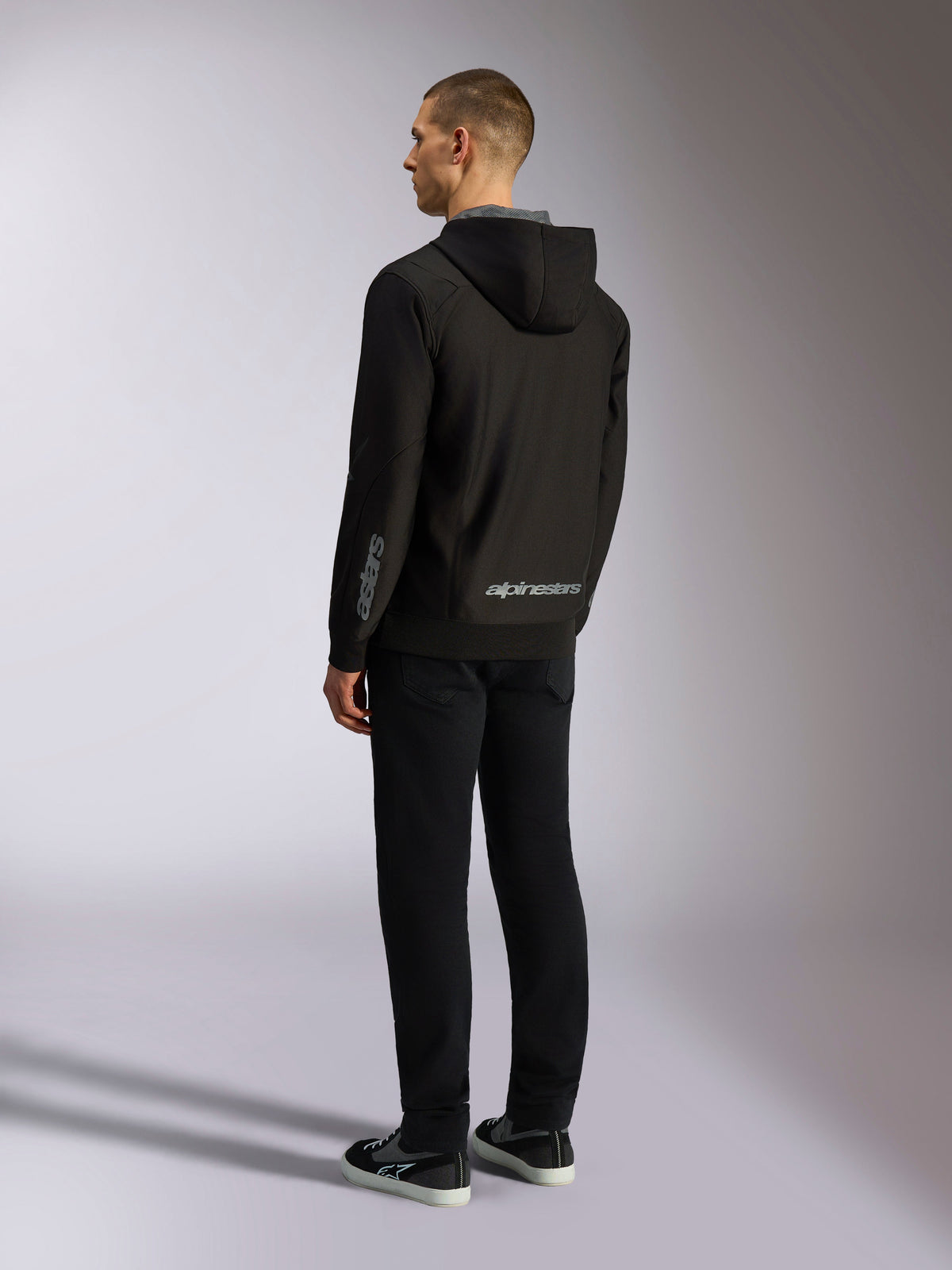 Alpinestars Sessions V3 Hoodie, streetwear casual motorsport, nero con scritta grigia sulla parte bassa della schiena e sull'avambraccio, felpa in pile di poliestere con zip frontale e cappuccio foderato in rete, vista posteriore su modello, design atletico moderno