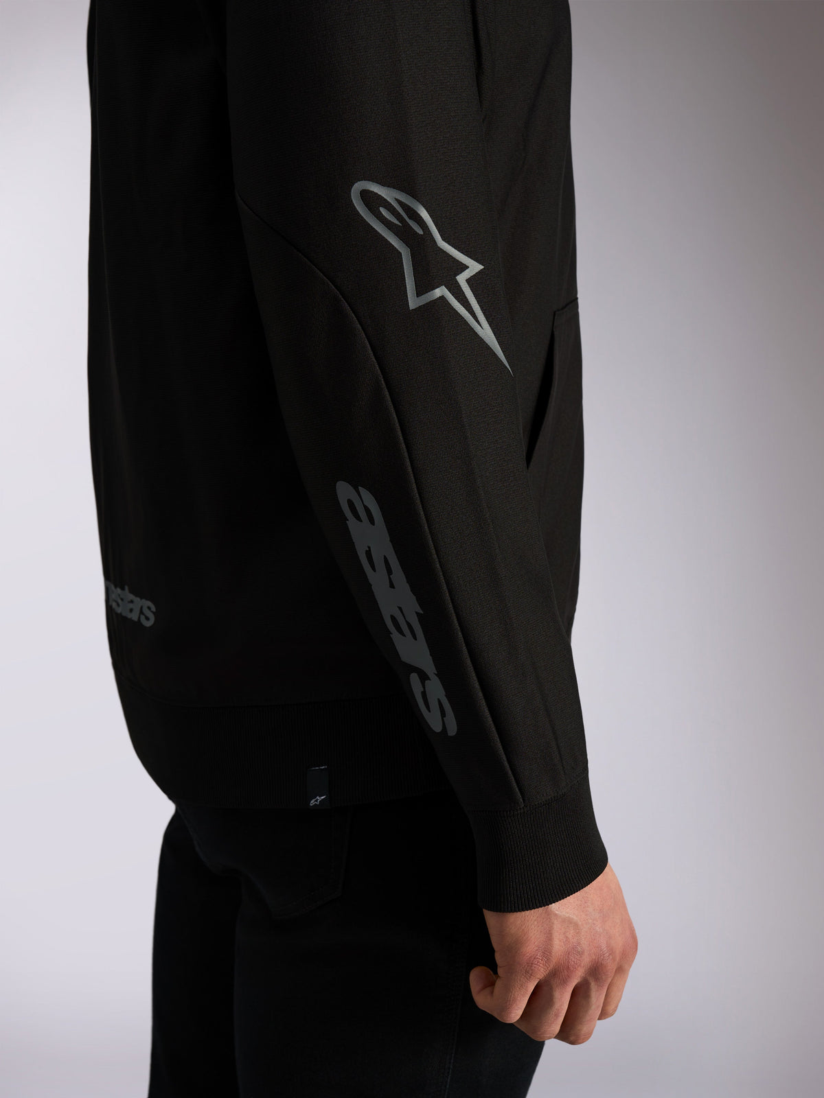 Alpinestars Sessions V3 Hoodie, felpa streetwear casual nera, primo piano della manica con logo Astars grigio sul gomito e scritta sull'avambraccio, polsini a coste, design ispirato al motorsport
