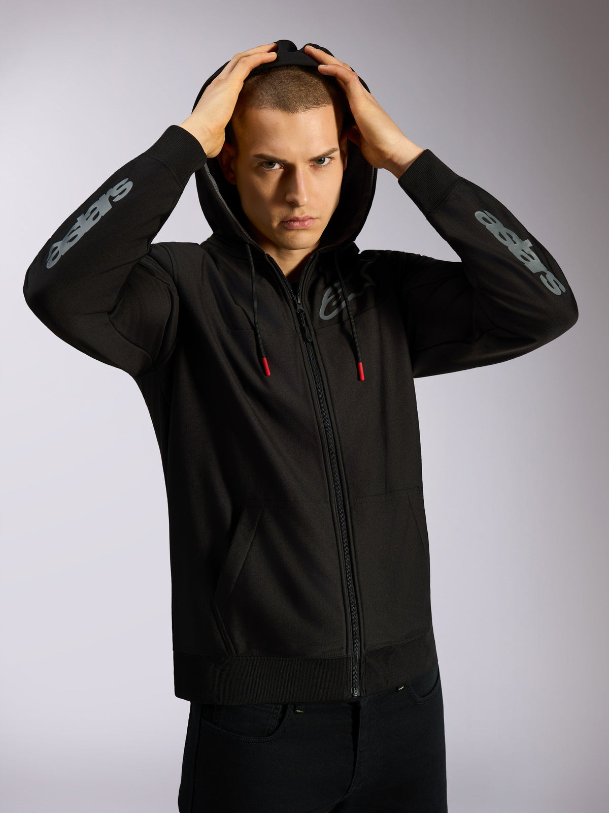 Alpinestars Sessions V3 Hoodie, felpa nera con zip integrale, logo Astars grigio sugli avambracci, cappuccio foderato in rete con cordini dalle punte rosse, streetwear casual ispirato al motorsport
