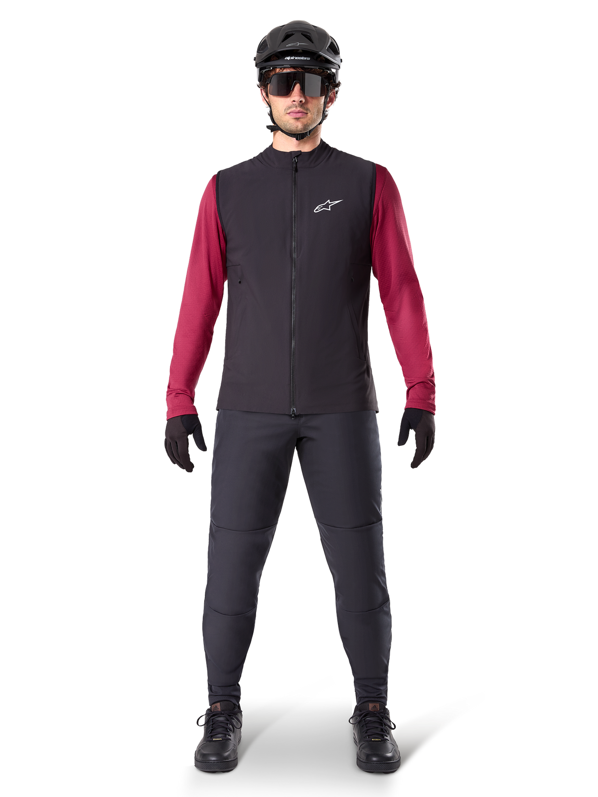 Gilet Termico Alpinestars A-Dura, gilet da ciclismo nero indossato sopra una maglia a maniche lunghe bordeaux, abbinato a pantaloni da MTB grigio scuro, casco e occhiali da sole neri, abbigliamento tecnico da mountain bike per climi freddi