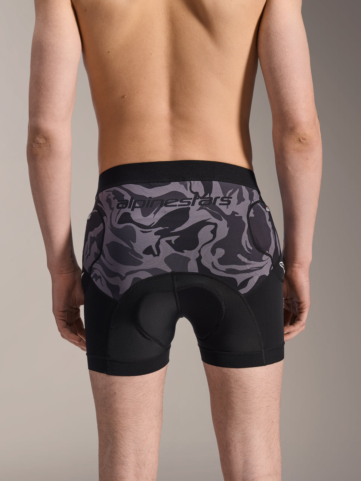Alpinestars A-Motion Plasma Protection Boxers, pantaloncini protettivi MTB, Black Camo, vista posteriore indossata da un modello, con logo Alpinestars su un pannello in mesh mimetico, fondello integrato e tasche per protezione fianchi, strato base traspirante per ciclismo fuoristrada