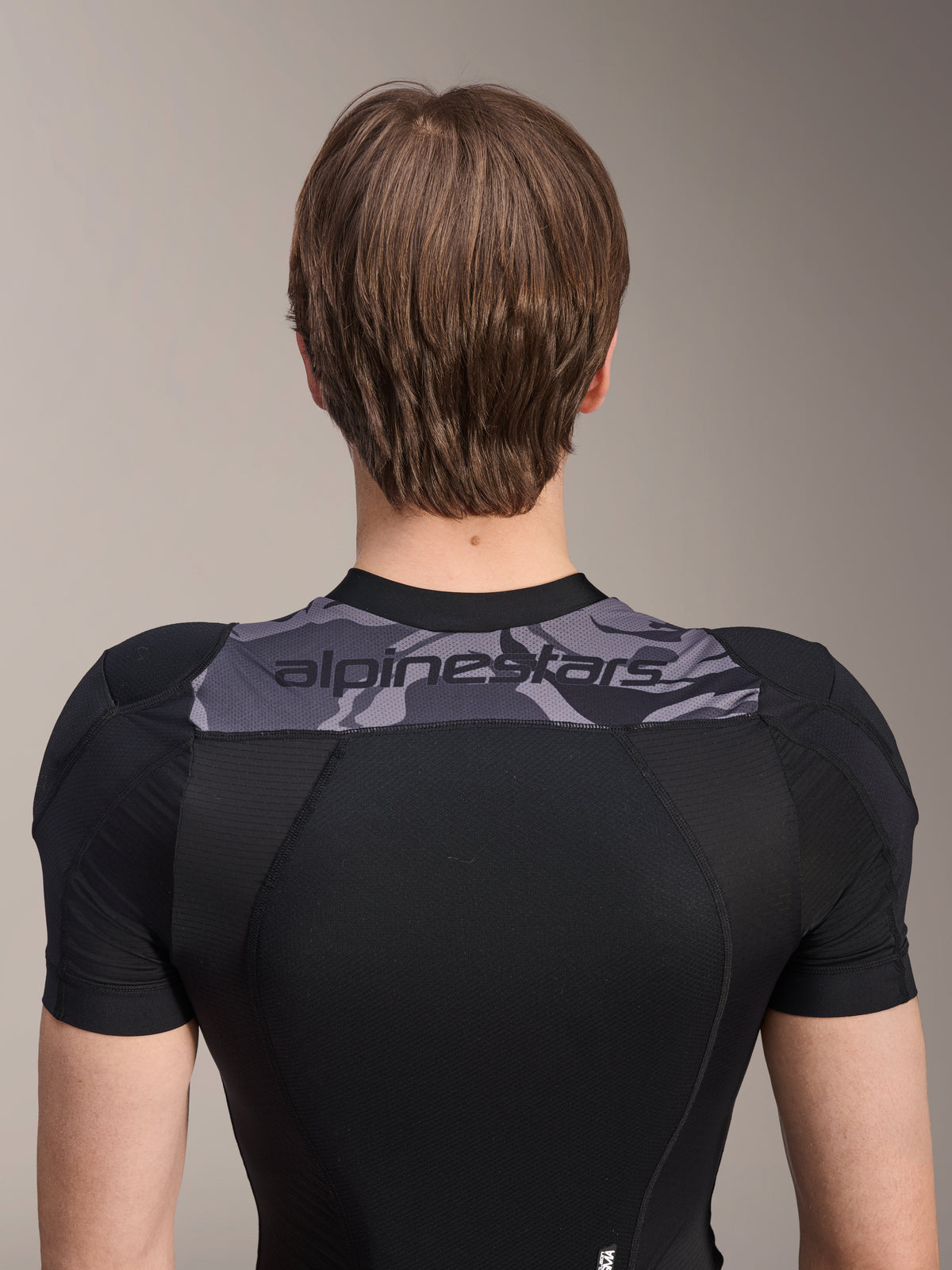 Alpinestars A-Motion Plasma Protection Jacket - Manica Corta, vista posteriore della parte superiore del busto, nero con pannello camo grigio sulle spalle e logo Alpinestars, struttura in mesh elasticizzato traspirante per protezione MTB