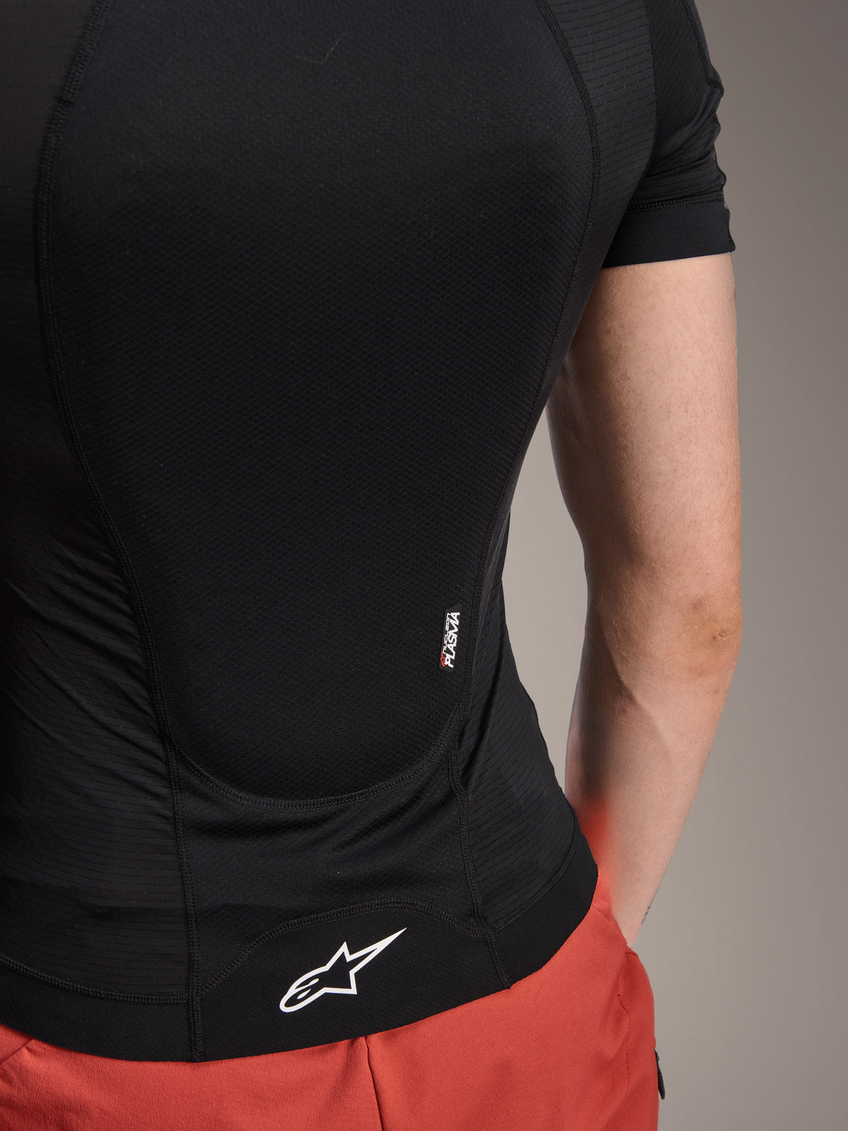 Giacca protettiva Alpinestars A-Motion Plasma - a maniche corte, Black Camo, dettaglio della vista posteriore con marchio Nucleon PLASMA e logo Alpinestars bianco sull'orlo, costruzione in rete elasticizzata traspirante per protezione MTB