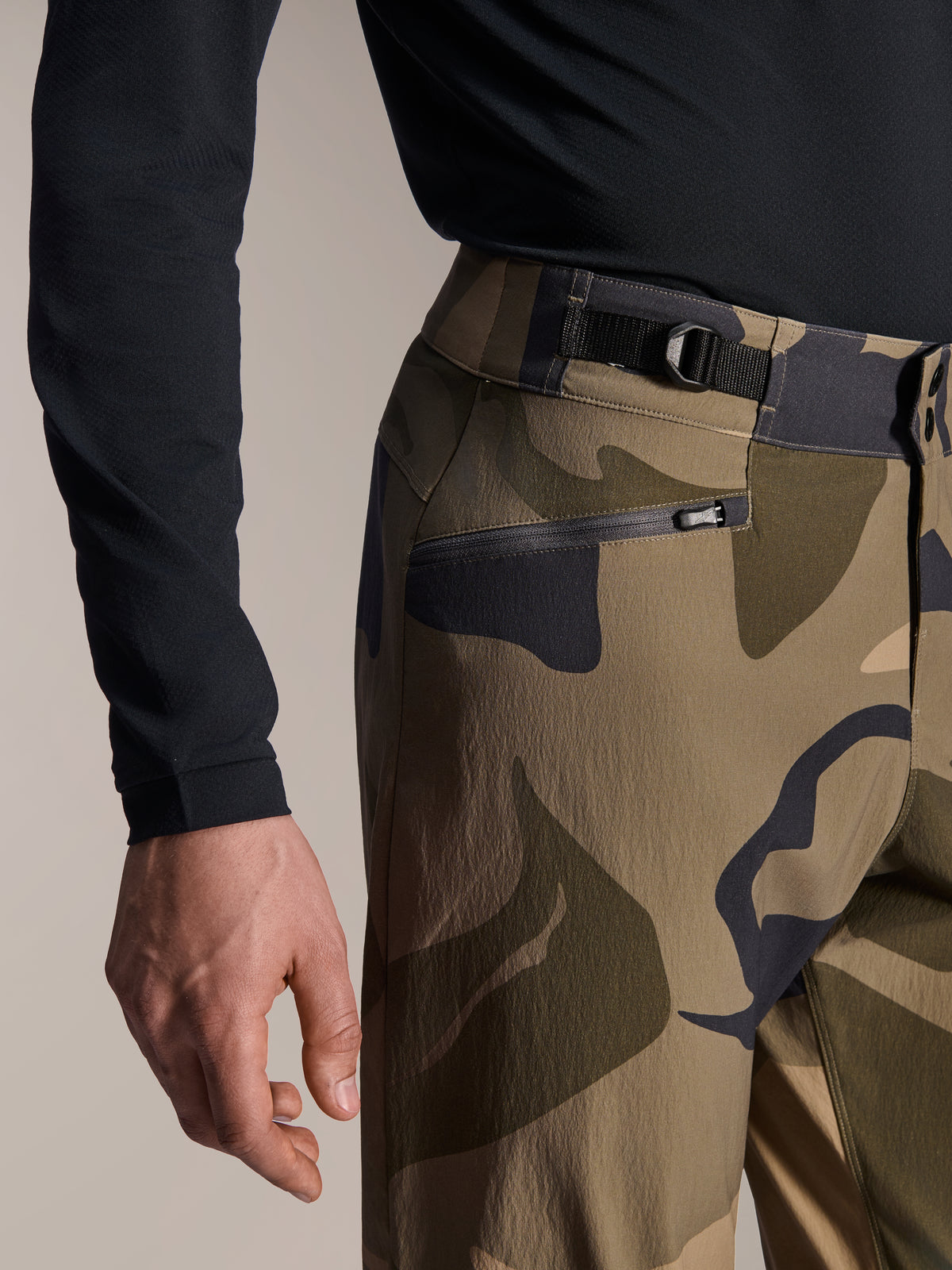 Pantaloni Alpinestars A-Dura Camo, pantaloni da MTB, mimetico marrone, vista ravvicinata della cinghia di regolazione laterale in vita e della tasca con cerniera foderata in rete, tessuto resistente elasticizzato in 2 direzioni per mountain bike