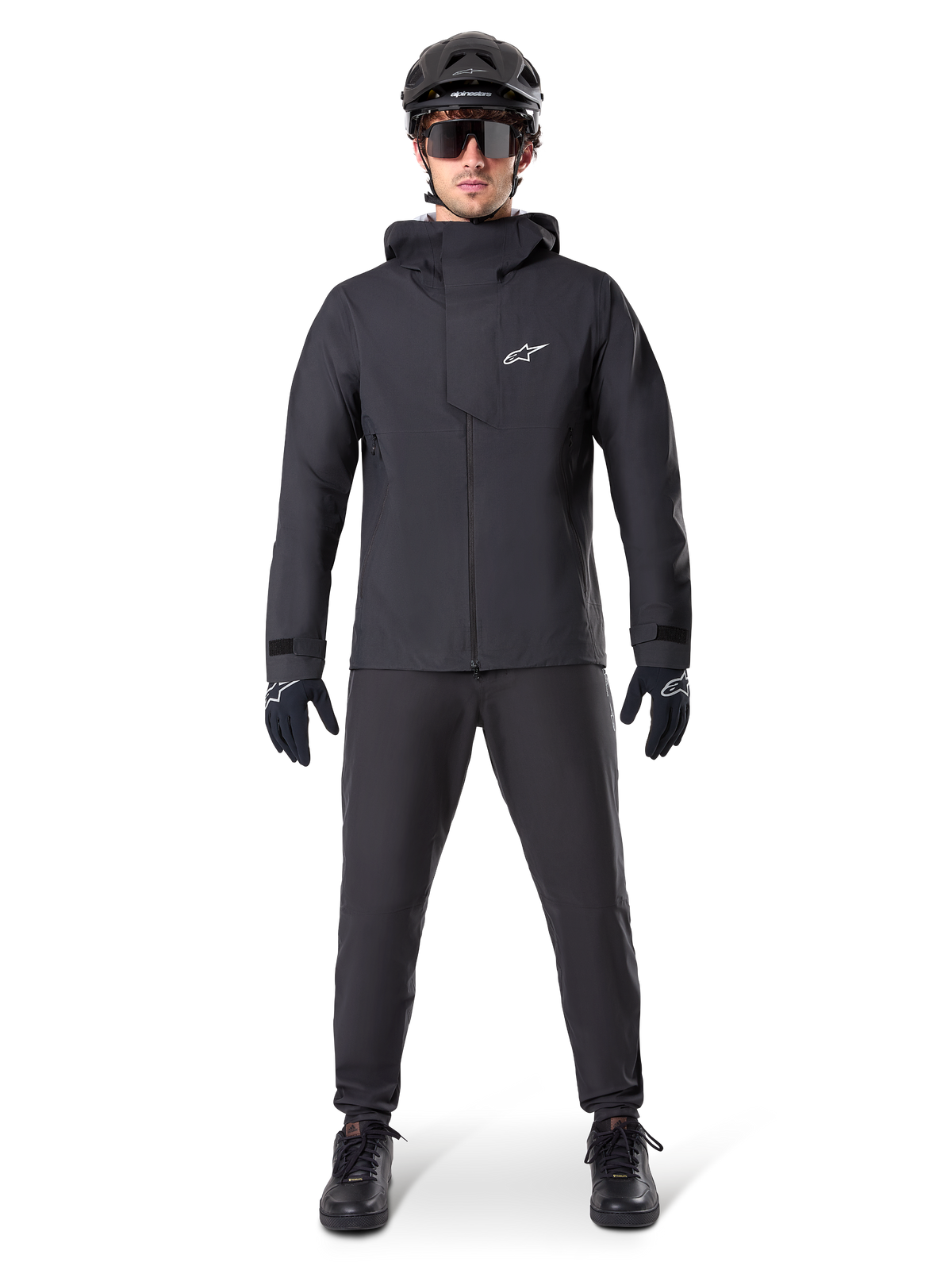 Pantaloni impermeabili Alpinestars A-Dura, pantaloni da MTB neri, indossati come parte di un set completo di abbigliamento da mountain bike total black che include giacca tecnica impermeabile, casco nero, occhiali da sole e guanti, progettati per la guida fuoristrada in condizioni di pioggia.