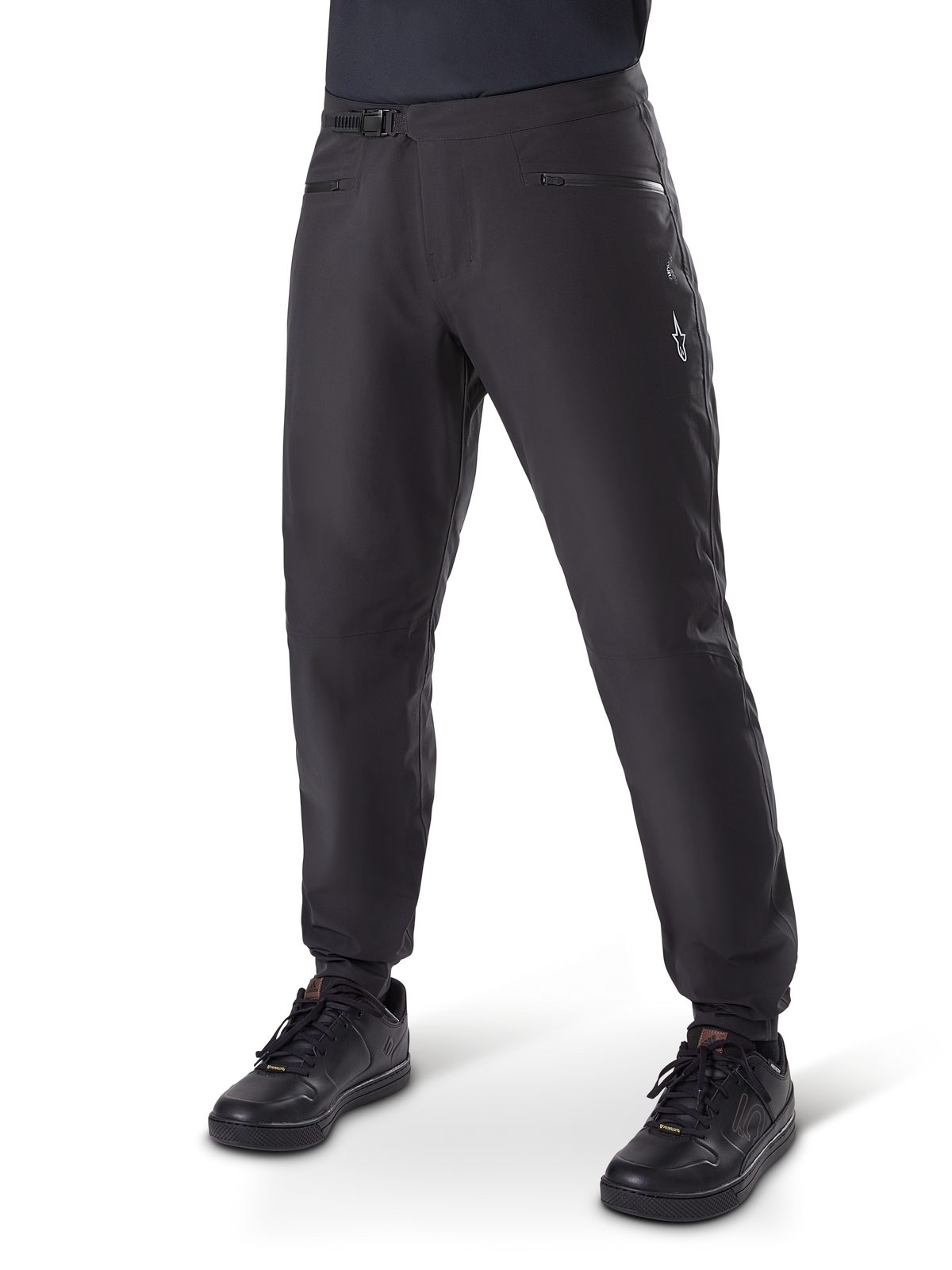 Alpinestars A-Dura Waterproof Pants, pantaloni da ciclismo MTB, nero, con chiusura a cricchetto in vita, tasche con cerniera e logo Astars bianco sulla coscia, mostrati con scarpe da ciclismo nere per il trail riding in ogni condizione meteorologica