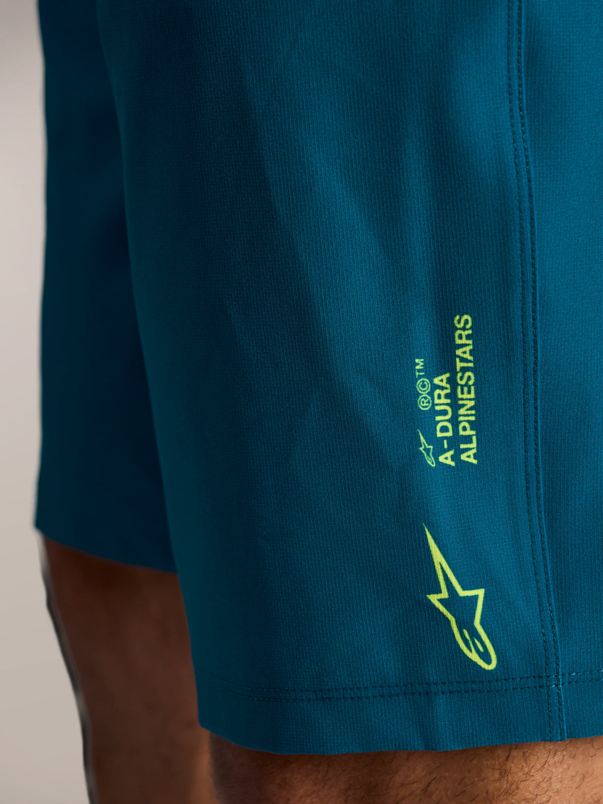 Pantaloncini MTB A-Dura Ride blu-verde, con branding laterale e logo Alpinestars verde lime su tessuto elasticizzato.