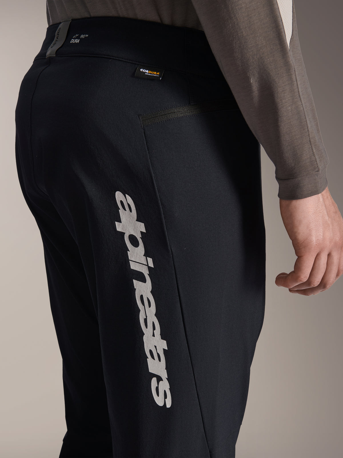 Pantaloni Alpinestars A-Dura Elite, pantaloni da mountain bike neri, vista laterale con grande logo Alpinestars verticale sulla gamba, etichetta in tessuto Cordura e tasca laterale con zip, abbigliamento tecnico da ciclismo per il fuoristrada