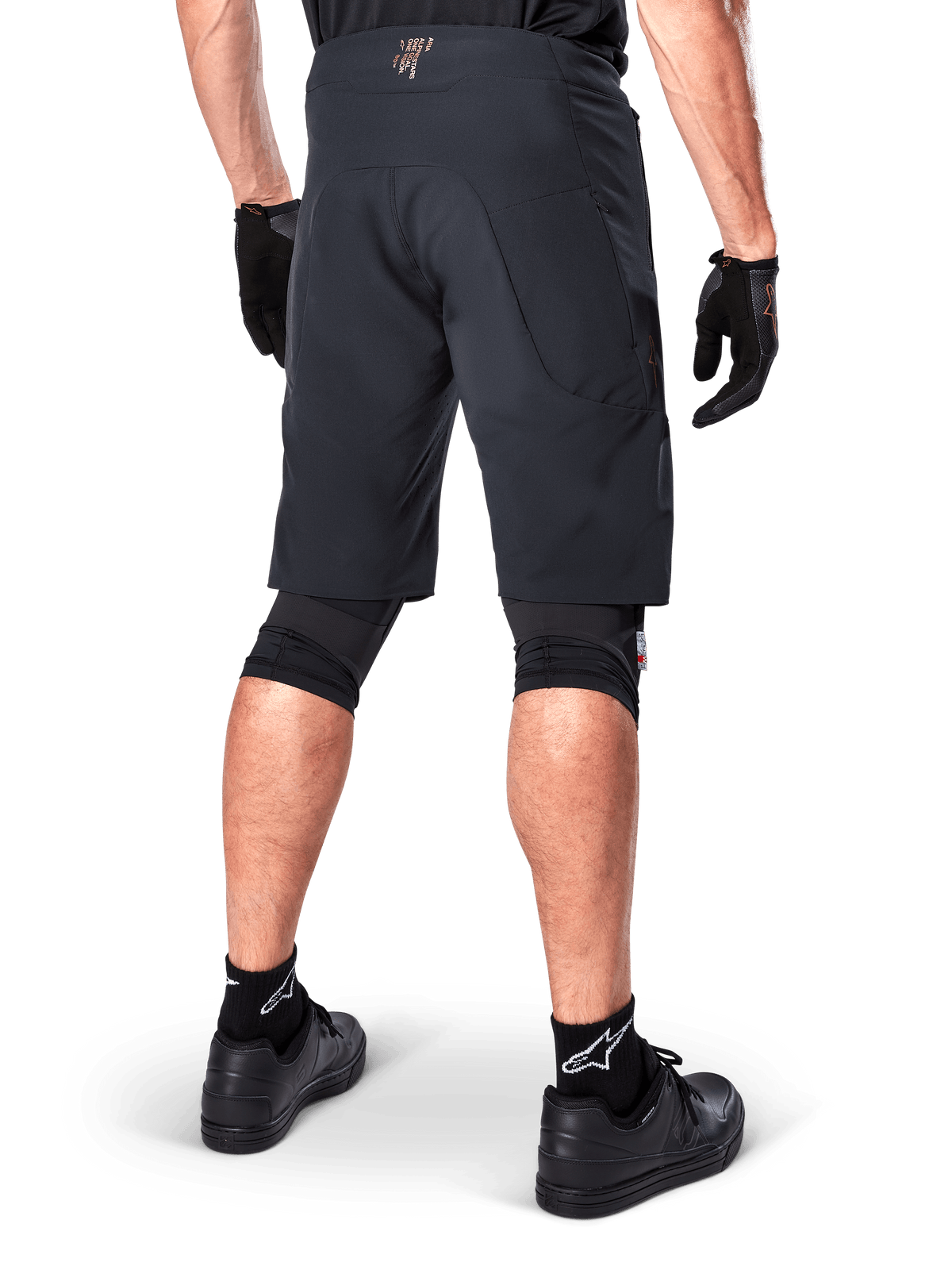 Vista posteriore di un rider che indossa i pantaloncini Alpinestars A-Aria Elite in nero, pantaloncini da mountain bike ad alte prestazioni, abbinati a guanti da ciclismo neri e scarpe nere, progettati per la flessibilità di movimento su percorsi fuoristrada