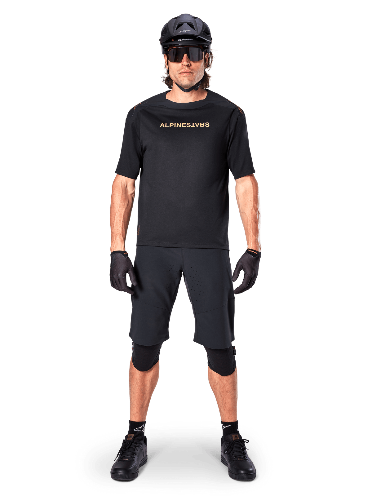 Ciclista di mountain bike con pantaloncini Alpinestars A-Aria Elite neri, abbinati a maglia a maniche corte coordinata, casco, guanti e ginocchiere neri, outfit completo per ciclismo fuoristrada