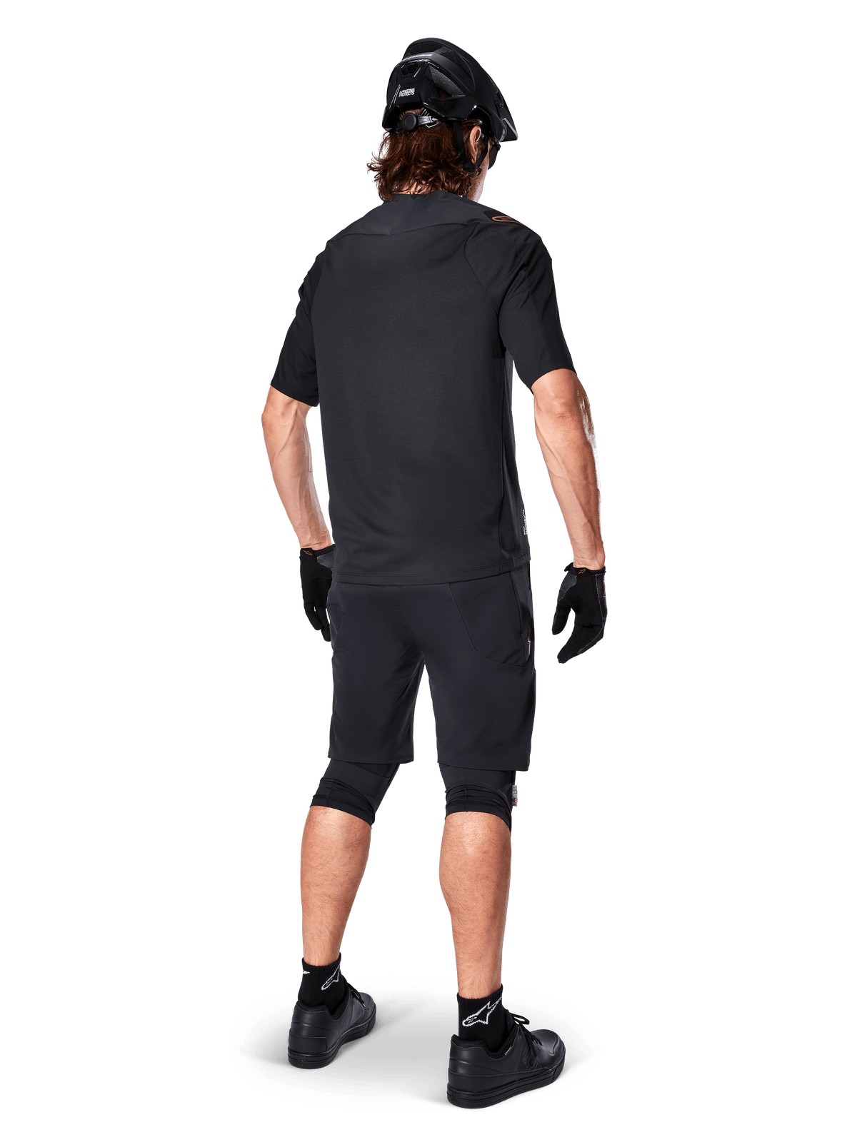 Vista posteriore di un mountain biker che indossa i pantaloncini Alpinestars A-Aria Elite neri, abbinati a una maglia a maniche corte coordinata, casco nero, guanti e scarpe da MTB, che mostra un outfit tecnico completo per il ciclismo off-road.