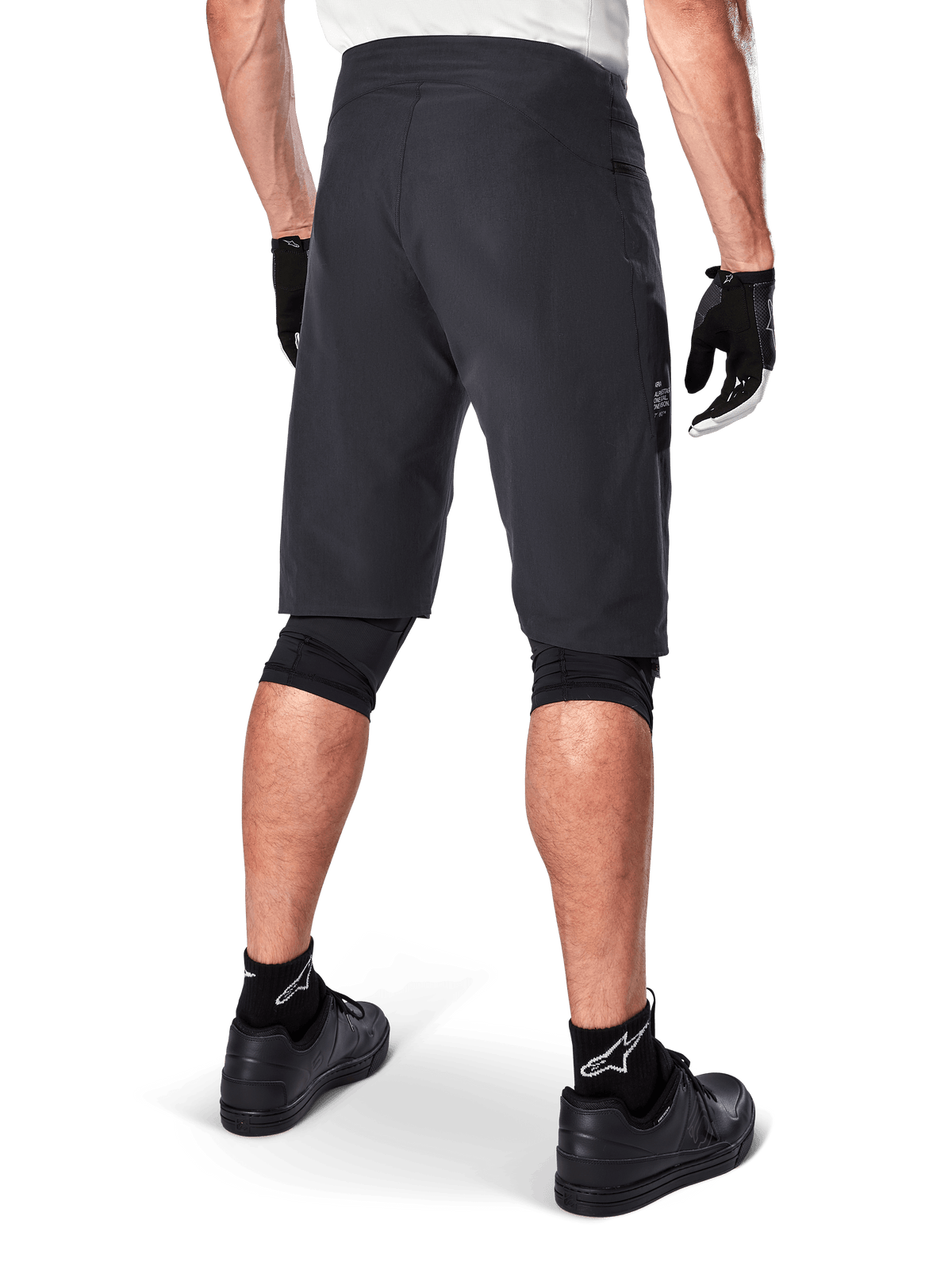 Alpinestars Pantaloncini A-Aria, pantaloncini da mountain bike, nero, vista posteriore che mostra la vestibilità performante e il design essenziale, indossati con guanti neri e calze con il logo Astars bianco, abbigliamento tecnico da ciclismo per fuoristrada