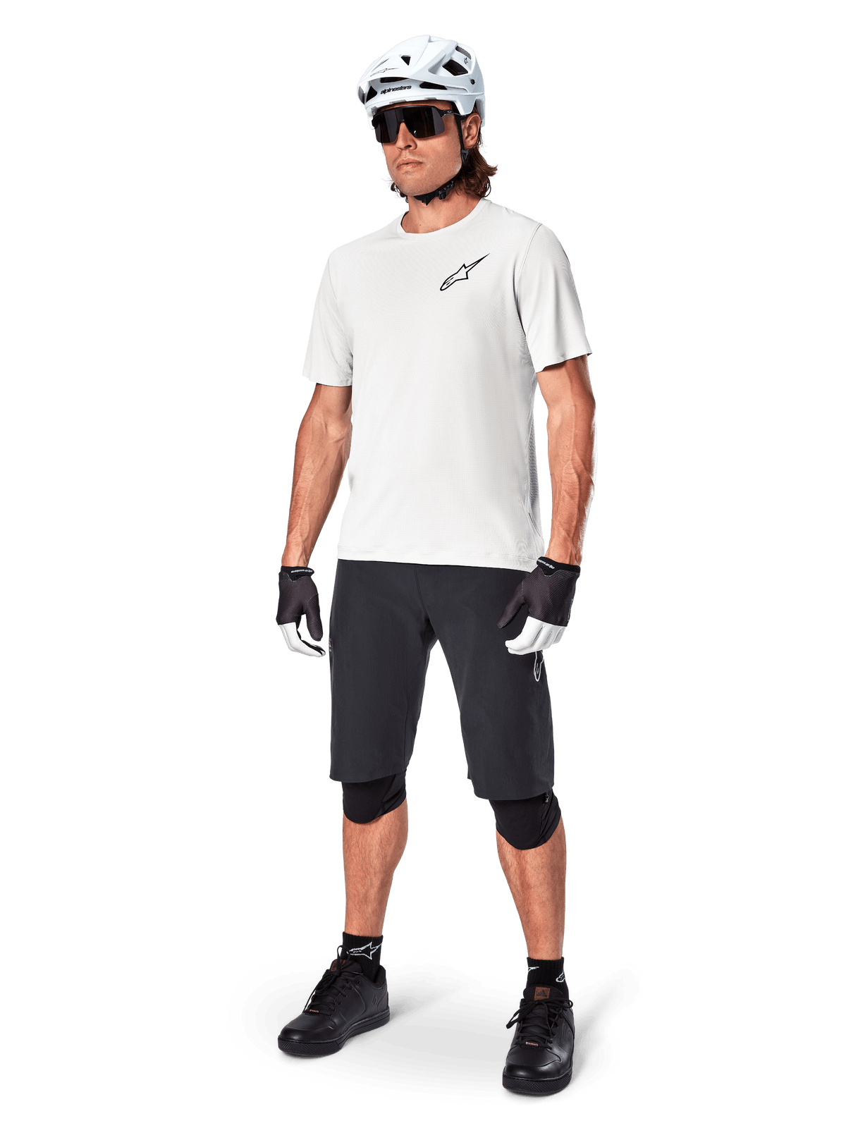 Mountain biker uomo con pantaloncini Alpinestars A-Aria, pantaloncini da ciclismo neri, abbinati a una maglia bianca a maniche corte, casco da mountain bike bianco e attrezzatura tecnica nera, outfit completo per il trail riding fuoristrada