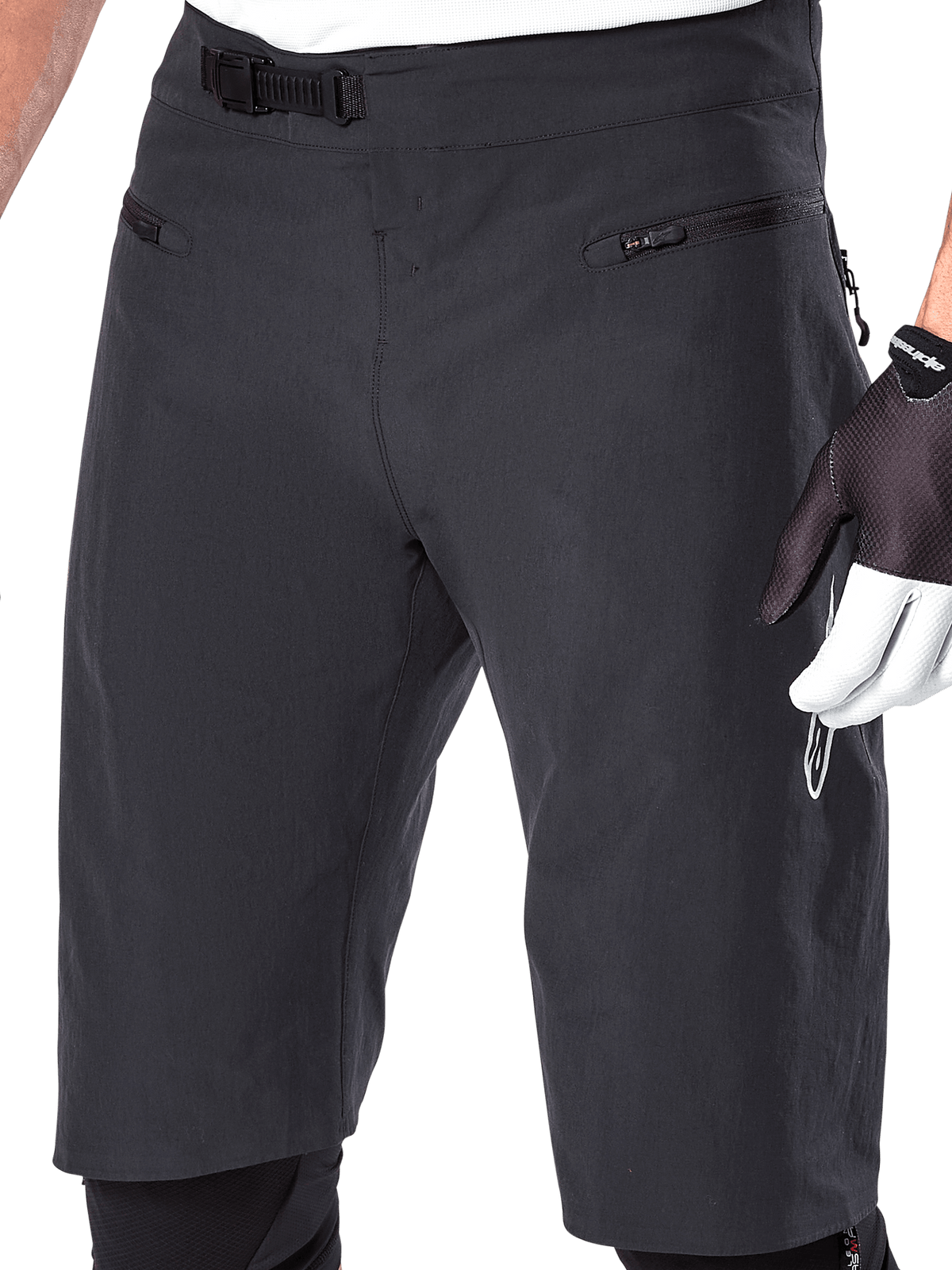 Alpinestars A-Aria Shorts, pantaloncini da mountain bike, nero, vista ravvicinata della vita anteriore e delle cosce che mostra il sistema di chiusura a cricchetto e le tasche con zip, indossati con guanti da ciclismo bianchi e neri, abbigliamento tecnico da trail